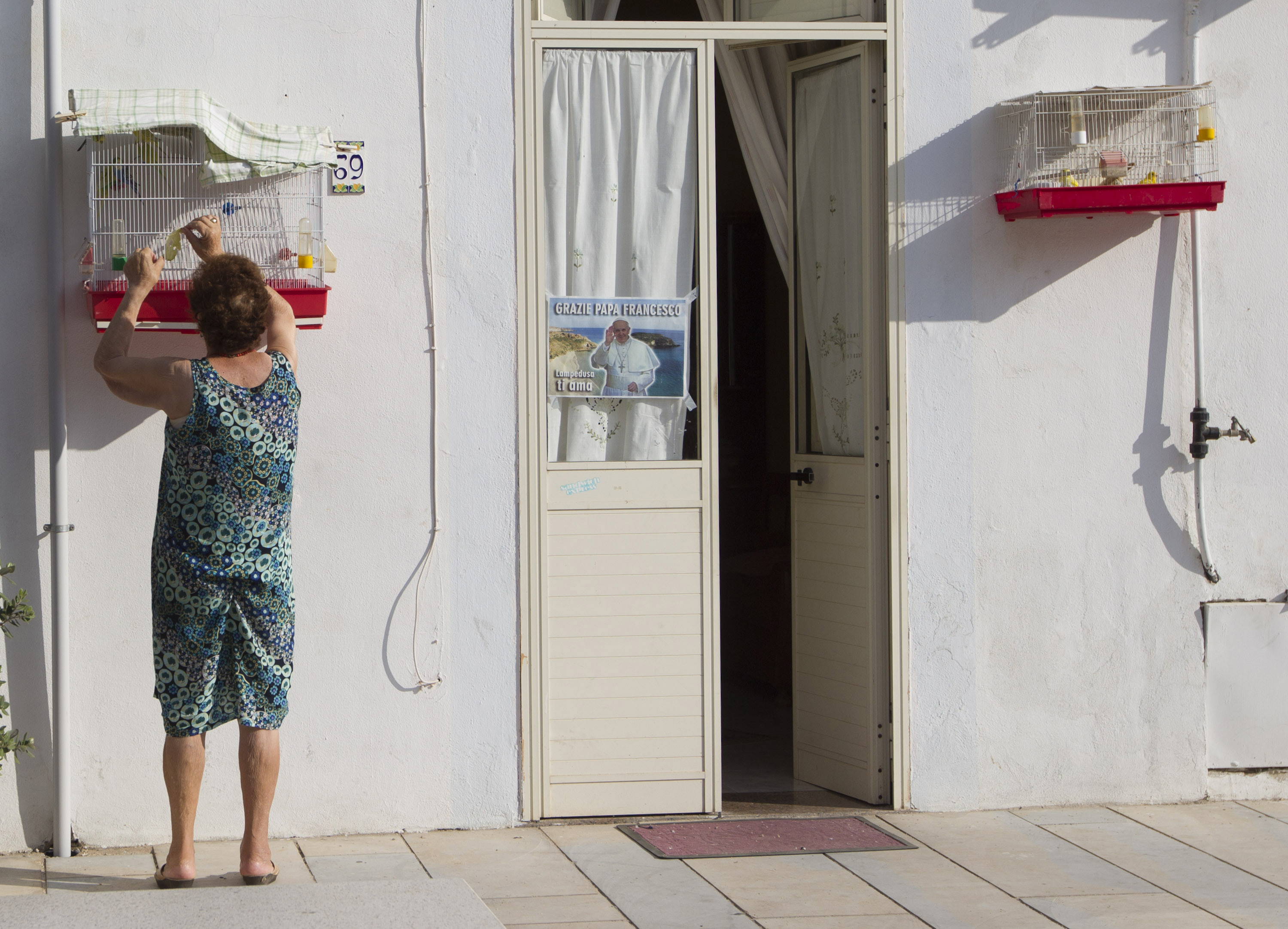 A woman cleans a birds cage outside her house in the tiny island of Lampedusa, southern Italy, Tuesday July 9, 2013 (AP Photo/Alessandra Tarantino)