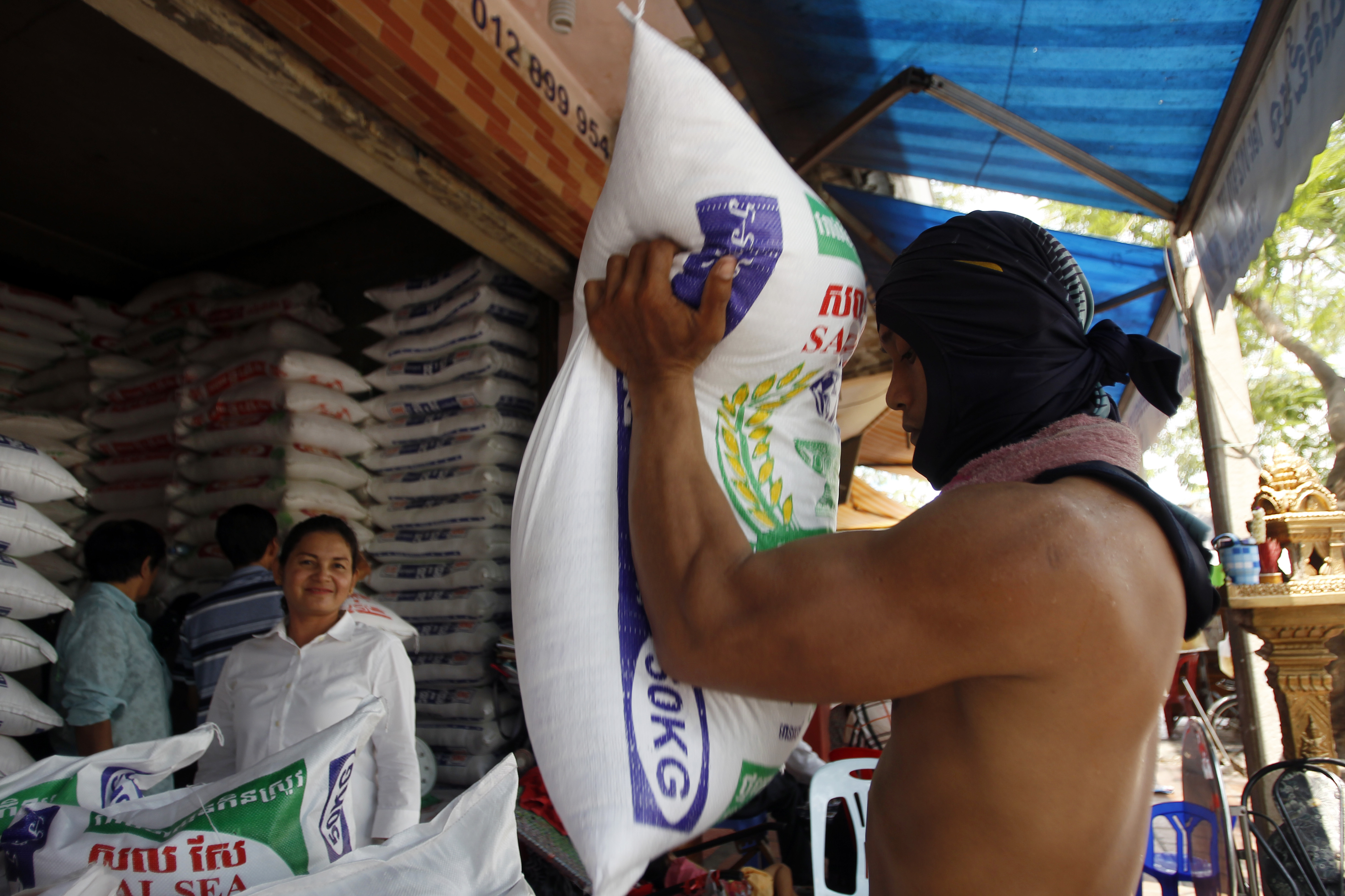A Cambodian worker, right, holds a rice sack as he prepares it to sell at a rice store in Phnom Penh, Cambodia, Saturday, April 27, 2019. Cambodia's close friend China agreed to buy 400,000 tons of rice from Cambodia for this year and next year. (AP Photo/Heng Sinith)