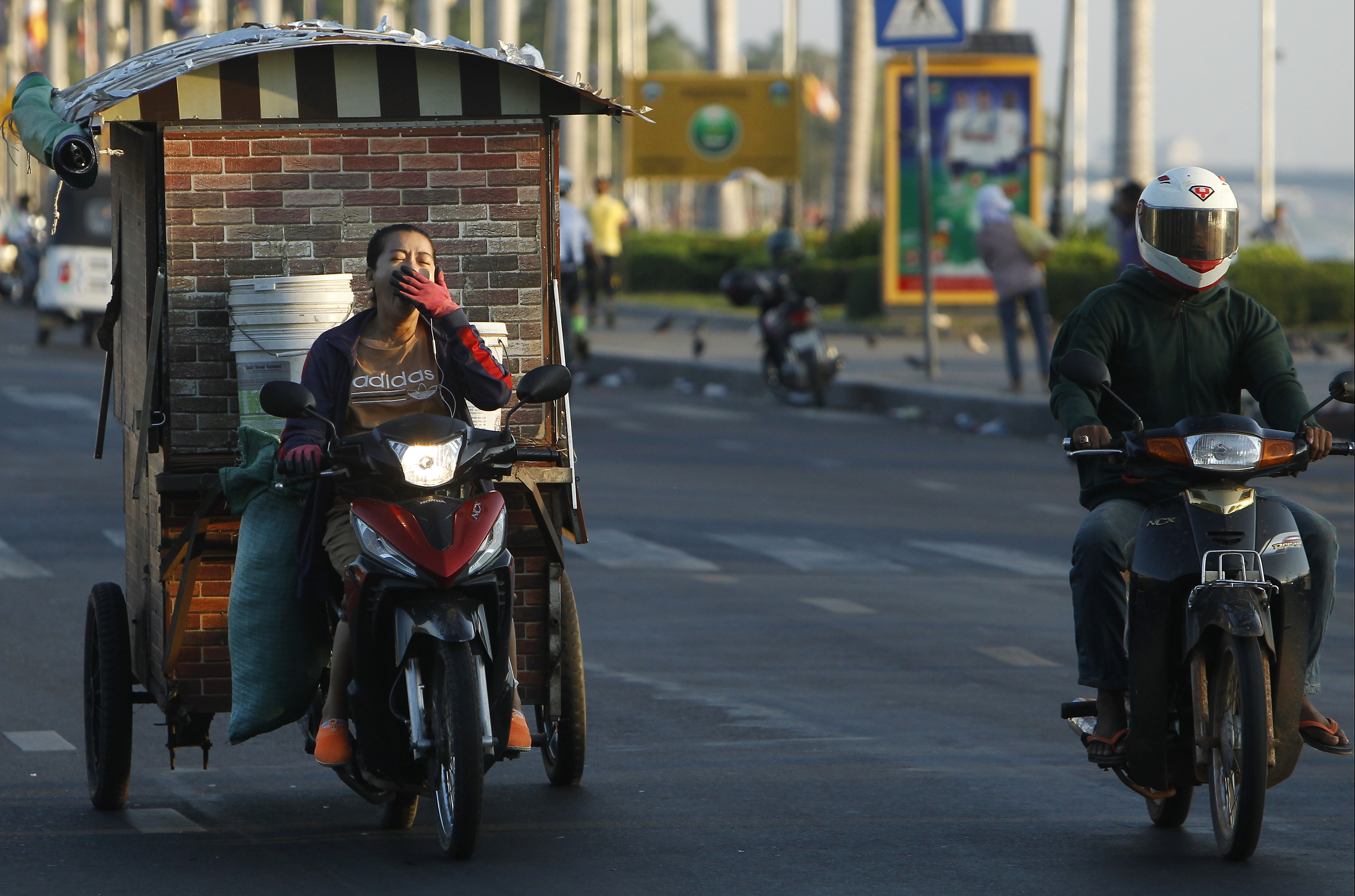 A deliver woman, left, yawns upon her drives a motor-cart in front of Royal Palace, in Phnom Penh, Cambodia, Monday, May 20, 2019. (AP Photo/Heng Sinith)