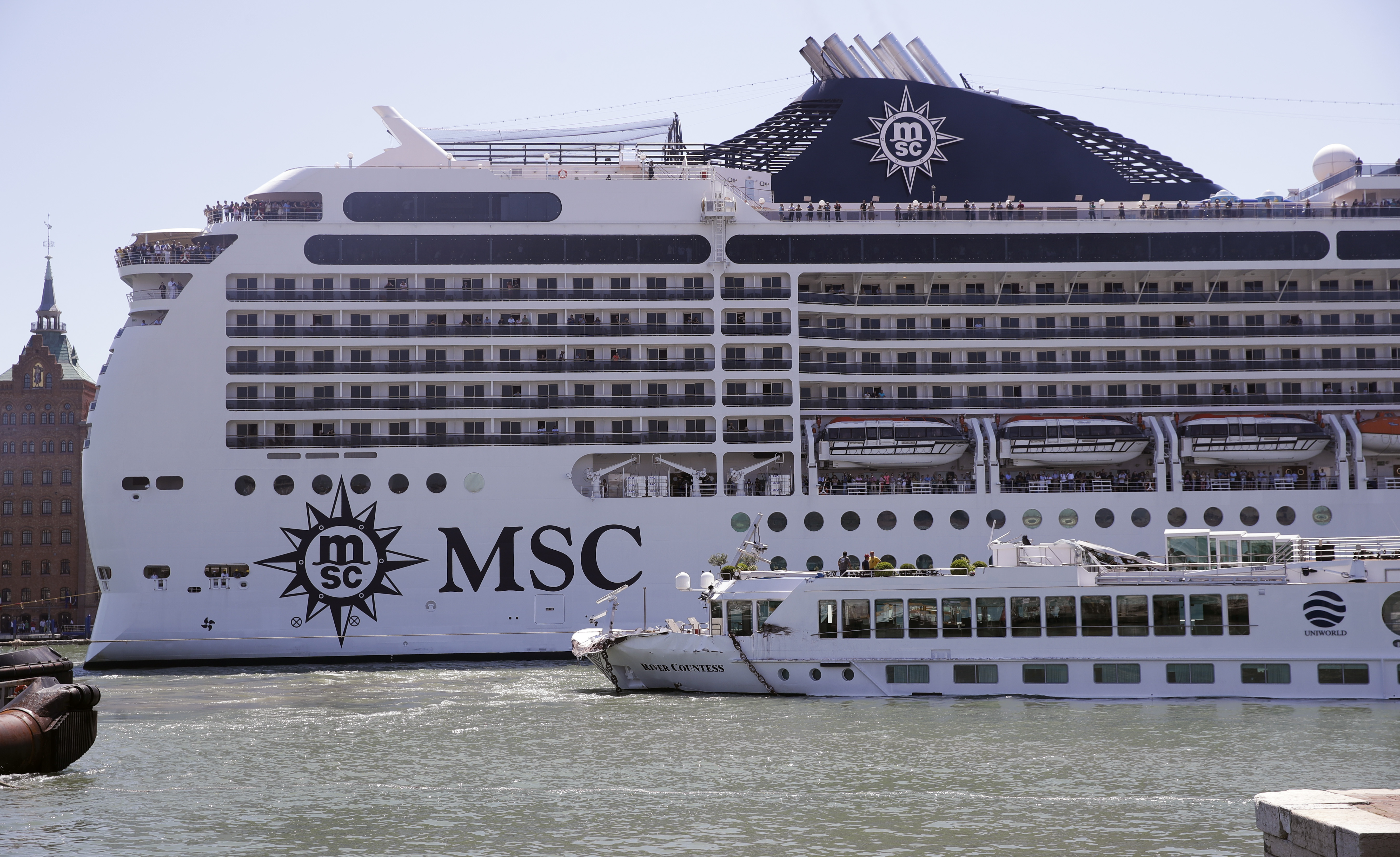 The MSC Magnifica cruise ship passes by the tourist boat, foreground, bottom right, that was struck by a towering cruiser, foreground right, in Venice, Italy, Sunday, June 2, 2019. The MSC Opera cruise ship has struck a dock and a tourist river boat on a busy canal in Venice. Italian media report that at least five people have been injured in the crash. (AP Photo/Luca Bruno)