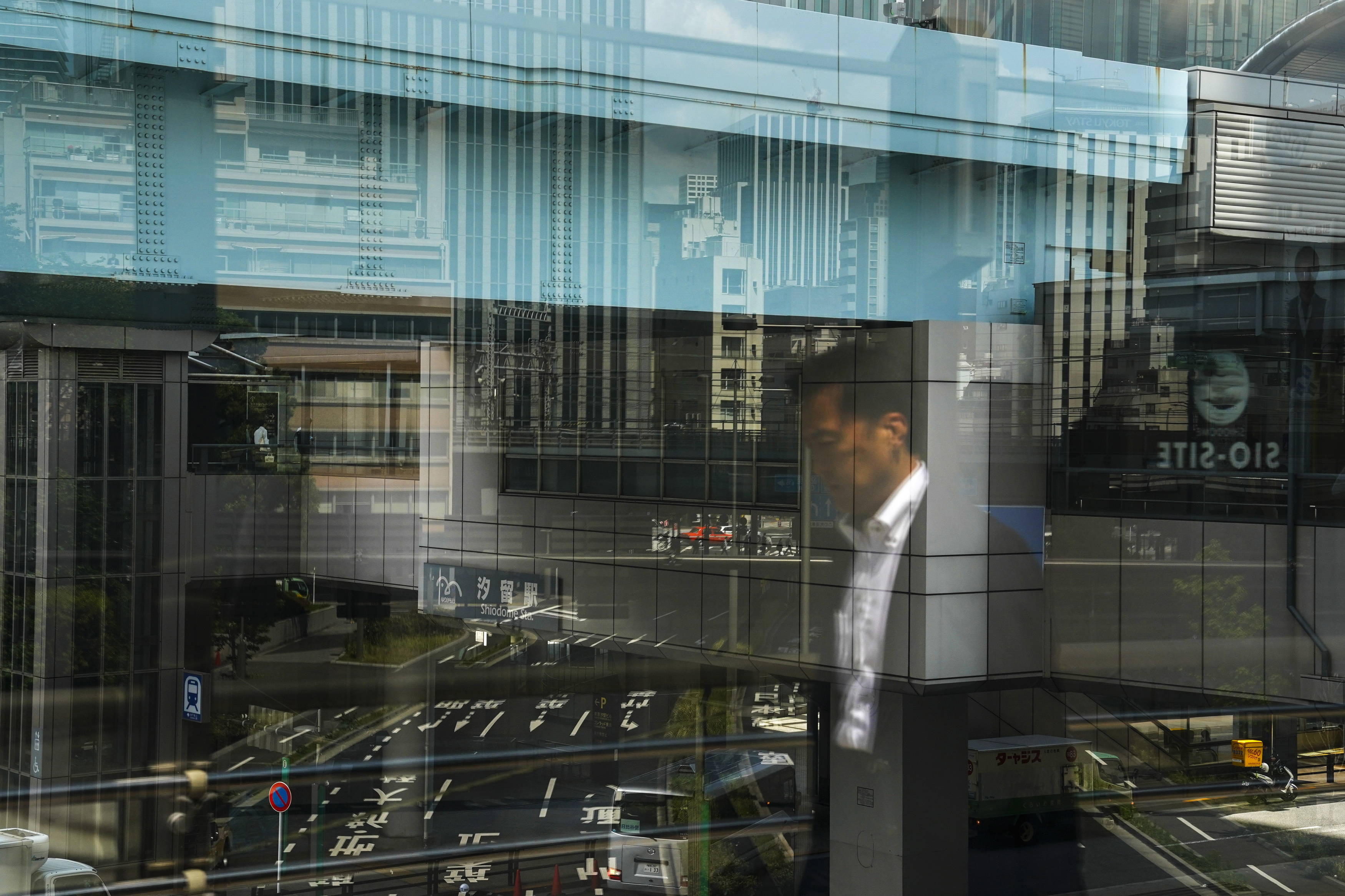 A commuter is reflected on a glass wall as he walks along the bridge Friday, May 17, 2019, in Shiodome district in Tokyo. (AP Photo/Jae C. Hong)