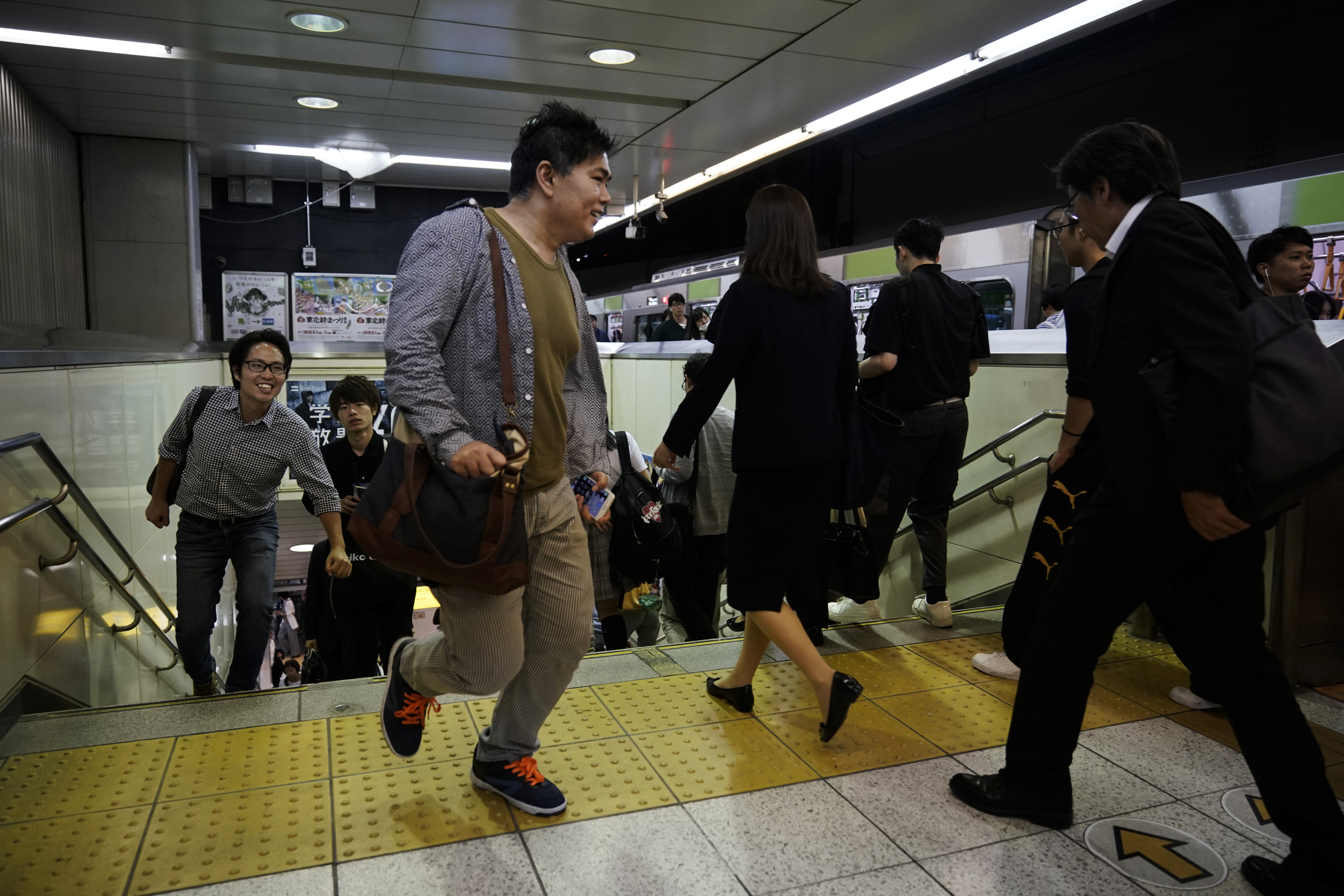 In this Friday, May 24, 2019, photo, two commuters run up the steps to catch a Yamanote Line train at Shinjuku Station in Tokyo. Want to take a glimpse of daily life in downtown Tokyo? Take a ride on the Yamanote loop line. For most Tokyoites, the line means an incredibly punctual and efficient transportation system for commuting. For tourists, it offers a glimpse into the life of ordinary people living in the city. (AP Photo/Jae C. Hong)