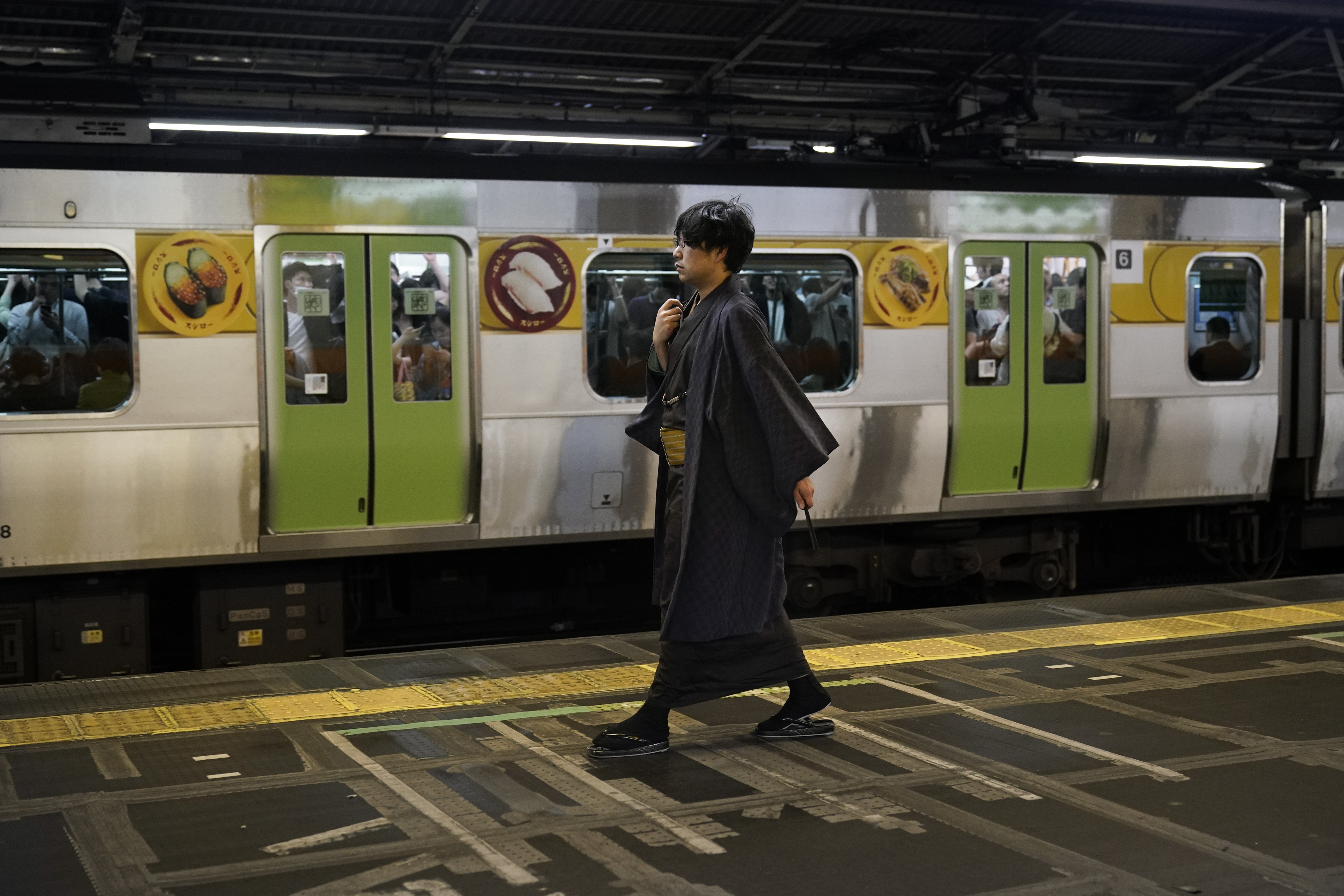 In this Saturday, May 25, 2019, photo, a young man wearing a traditional kimono walks past a packed Yamanote Line train at Shinjuku Station in Tokyo. Operated by the East Japan Railway Co., the Yamanote Line in Tokyo makes a loop around the center of the city, connecting 29 stations that include key stops such as Shinjuku, Shibuya and Ikebukuro. A complete loop of about an hour offers scenes of Japanese daily lives. (AP Photo/Jae C. Hong)
