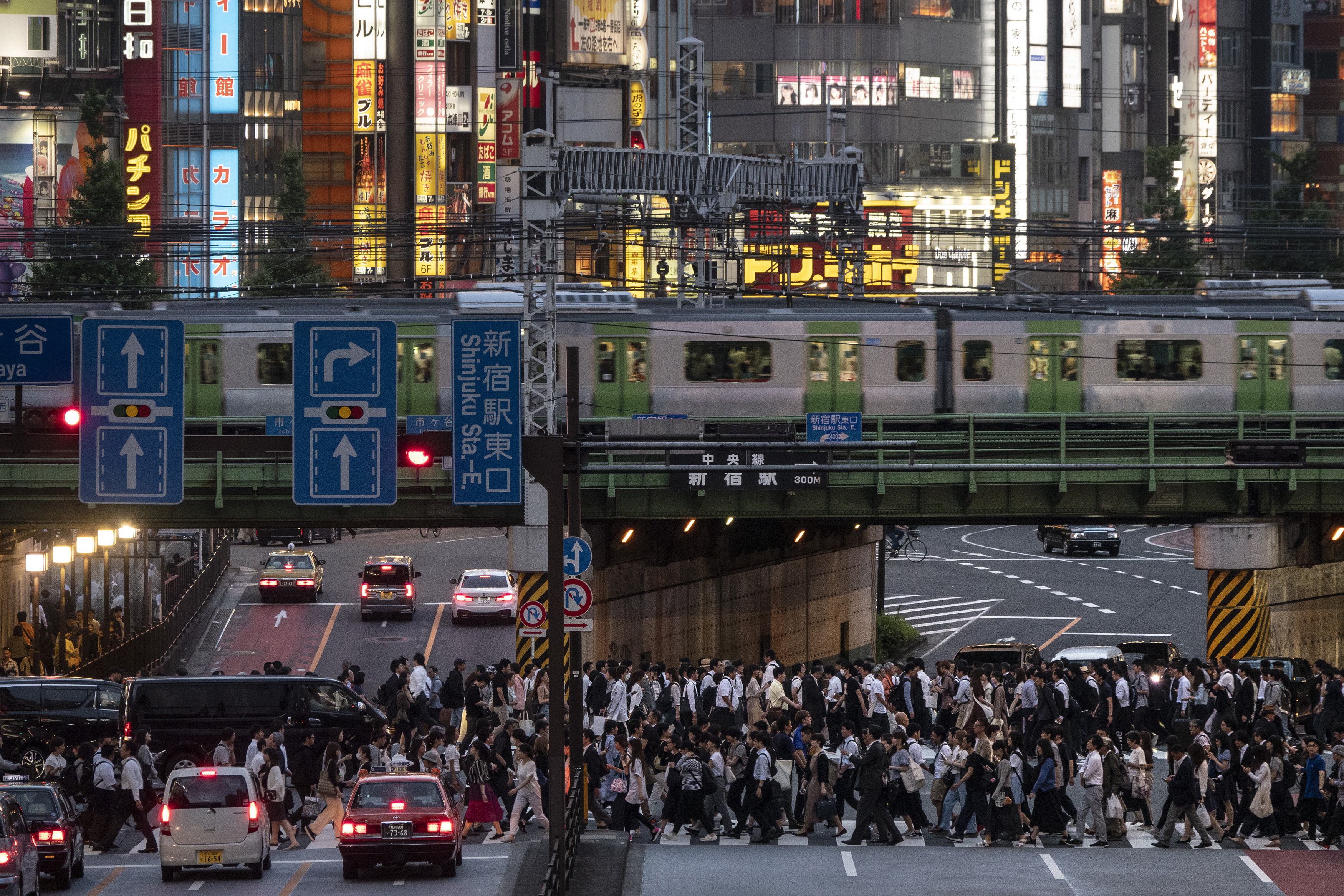 In this Tuesday, June 4, 2019, photo, a Yamanote Line train travels above commuters walking across the crossing during evening rush hours in the Shinjuku district of Tokyo. Operated by the East Japan Railway Co., the Yamanote Line in Tokyo makes a loop around the center of the city, connecting 29 stations that include key stops such as Shinjuku, Shibuya and Ikebukuro. A complete loop of about an hour offers scenes of Japanese daily lives. (AP Photo/Jae C. Hong)