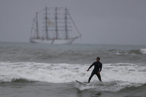 A surfer slides off a dying wave as he surfs in front of the BUP Union naval teaching ship, which was carrying the Pan Am Games torch, off the coast of Lima, Peru, Friday, July 26, 2019. In the Peruvian capital, where dozens of schools teach locals and tourists from around the world how to ride the waves at beaches with Hawaiian names, professional surfers from across the Americas are preparing to compete when the sport is featured for the first time in the Pan Am Games.(AP Photo/Rebecca Blackwell)