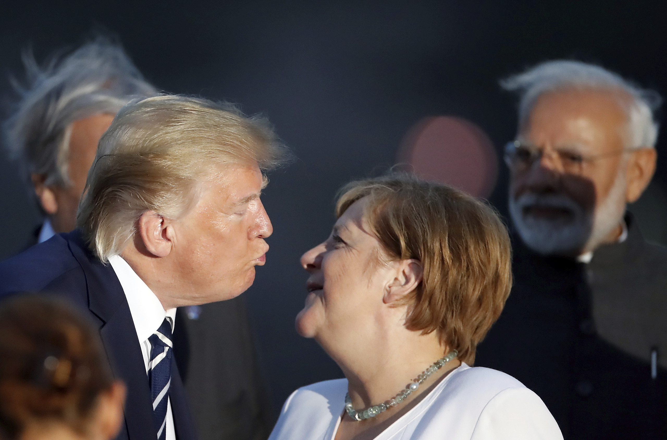 President Donald Trump kisses German Chancellor Angela Merkel during the G7 family photo Sunday, Aug. 25, 2019 in Biarritz. A top Iranian official paid an unannounced visit Sunday to the G-7 summit and headed straight to the buildings where leaders of the world's major democracies have been debating how to handle the country's nuclear ambitions. (Christian Hartmann, Pool via AP)