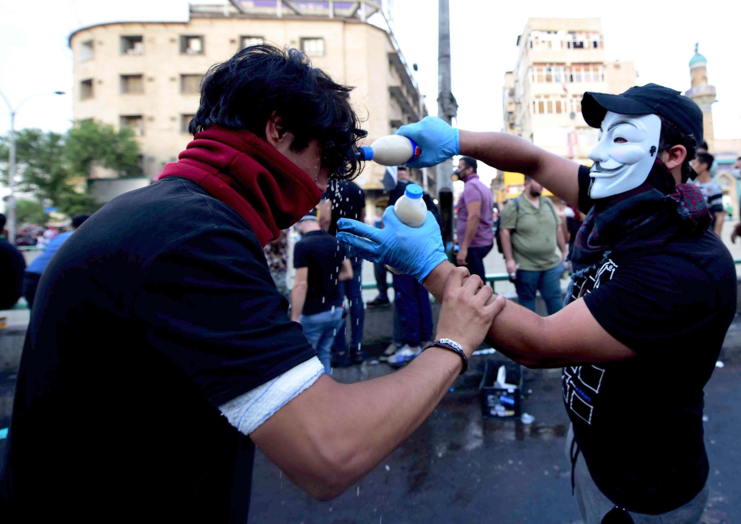 epa07954346 An Iraqi protester wearing mask helps a man after being affected by tear gas, which was dispensed by riot police during clashes with  protesters at al-Tahrir square, central Baghdad, Iraq, 27 October 2019. According to media reports, at least 63 people died during three days of violent clashes between security forces and people protesting against the government in Baghdad and southern Iraqi cities.  EPA/MURTAJA LATEEF