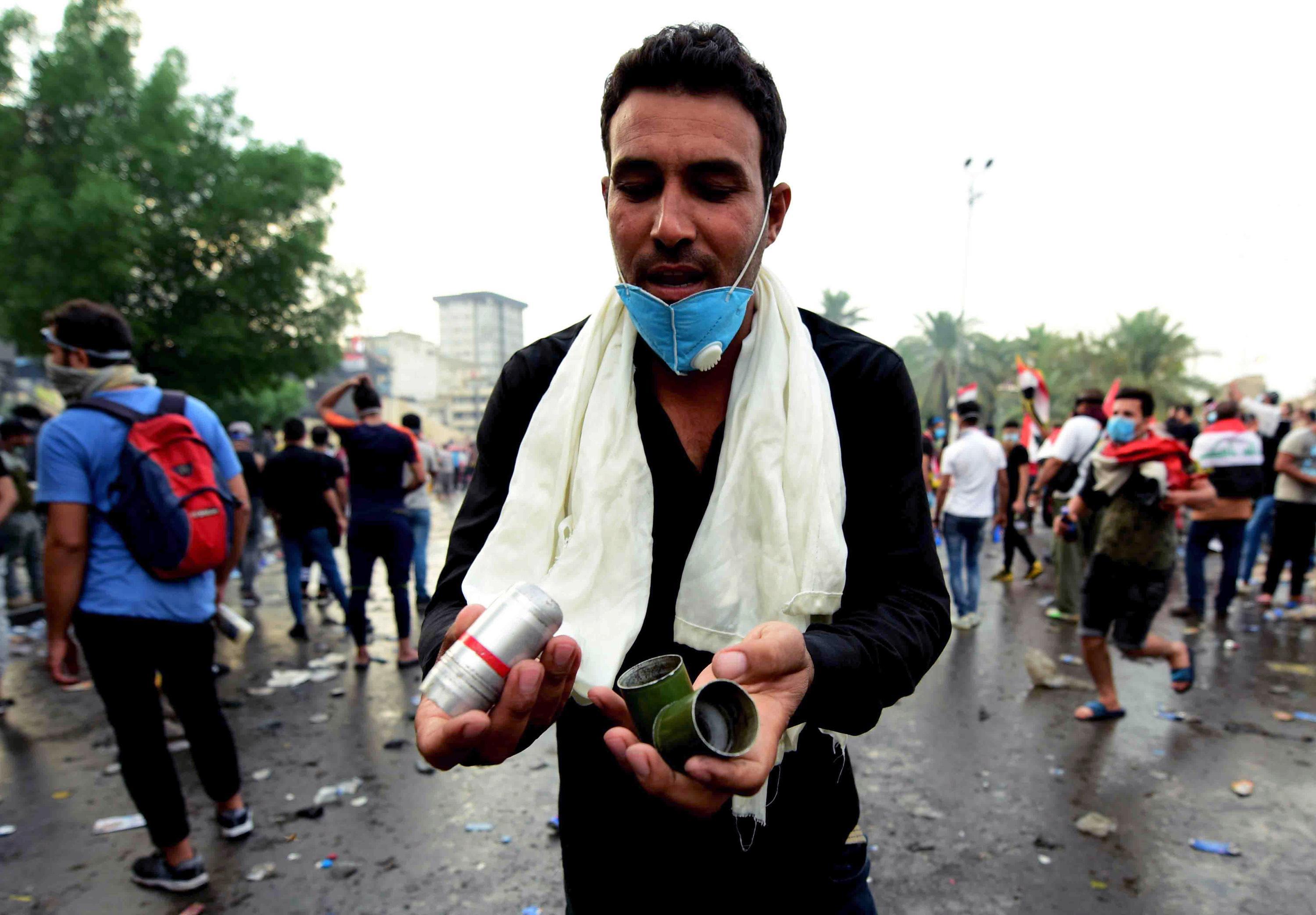 epa07954342 An Iraqi protester carries tear gas canisters which were dispensed by riot police during clashes with protesters at al-Tahrir square, central Baghdad, Iraq, 27 October 2019. According to media reports, at least 63 people died during three days of violent clashes between security forces and people protesting against the government in Baghdad and southern Iraqi cities.  EPA/MURTAJA LATEEF