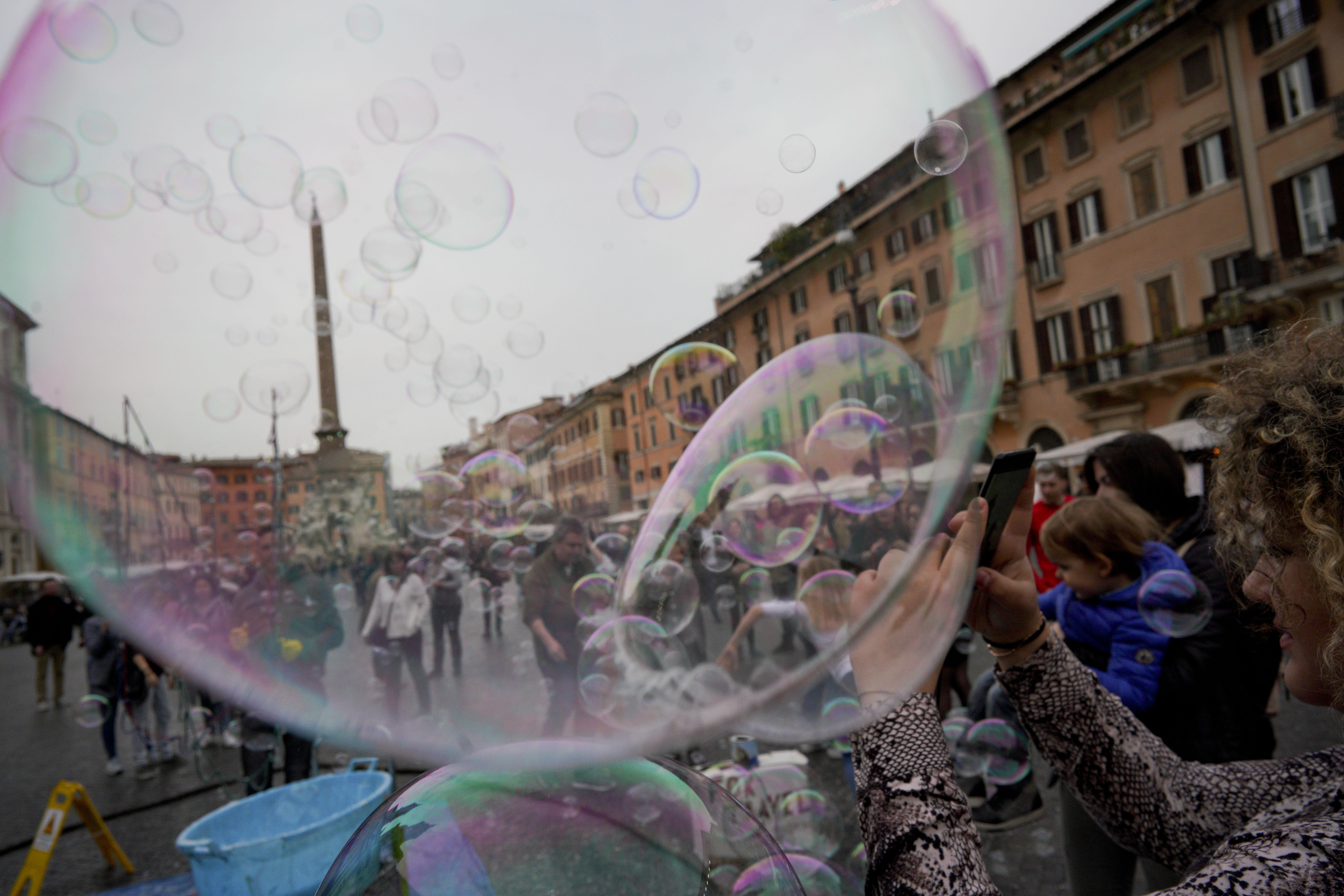 A woman takes pictures of soap bubbles made by a street artist in Rome's historical Piazza Navona square, Thursday, March 7, 2019. (AP Photo/Andrew Medichini)
