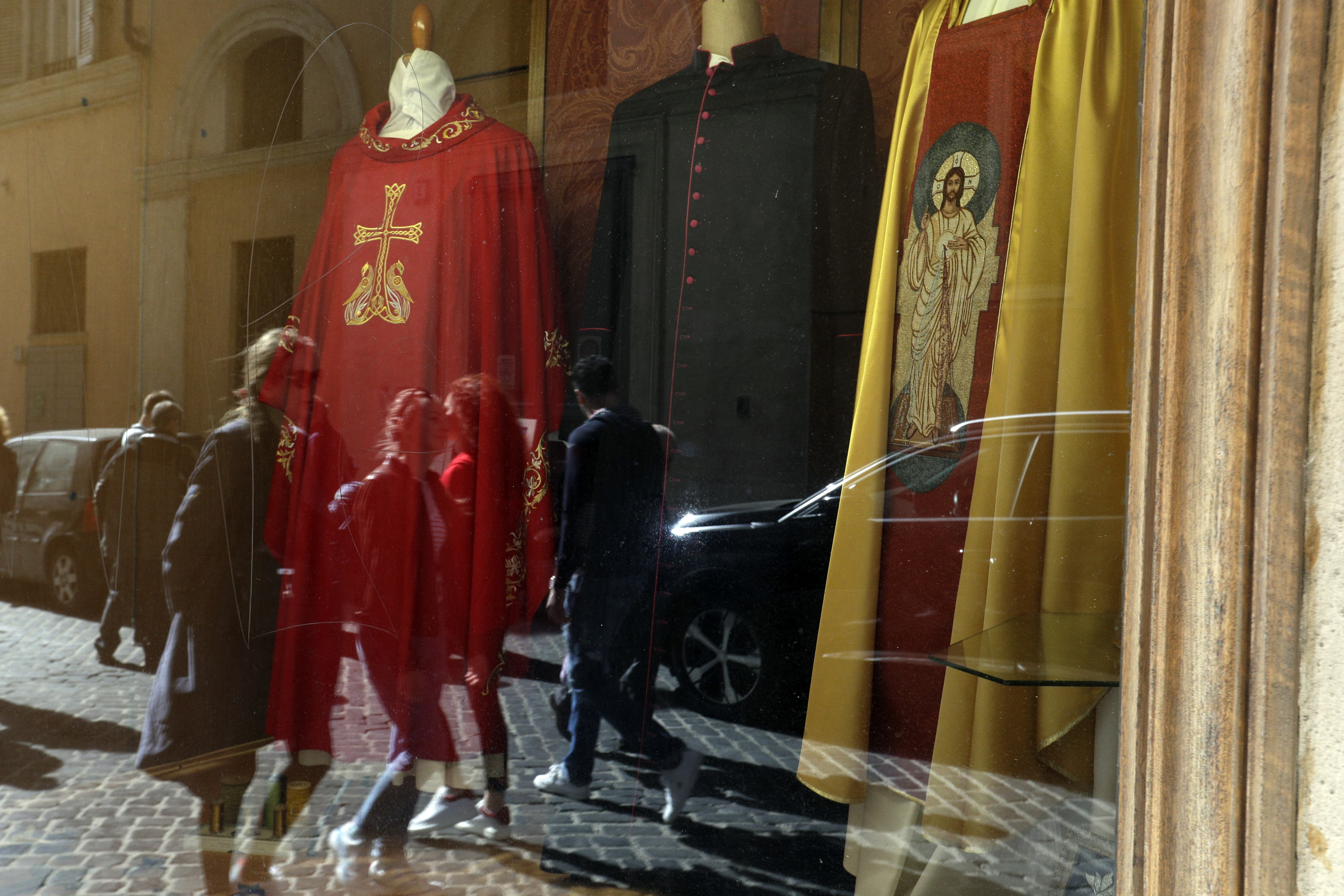 Passers by are reflected in the window of a clergy robes shop, in Rome, Thursday, March 7, 2019. (AP Photo/Gregorio Borgia)