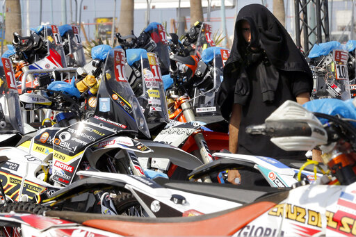 A visitor covers his head as he watches motorbikes parked in Dakar village, in Jiddah, Saudi Arabia, Saturday, Jan. 4, 2020. The Dakar Rally is swapping South America for Saudi Arabia. Created in 1977, the rally was raced across Africa until terror threats in Mauritania led organizers to cancel the 2008 edition. (AP Photo/Amr Nabil)