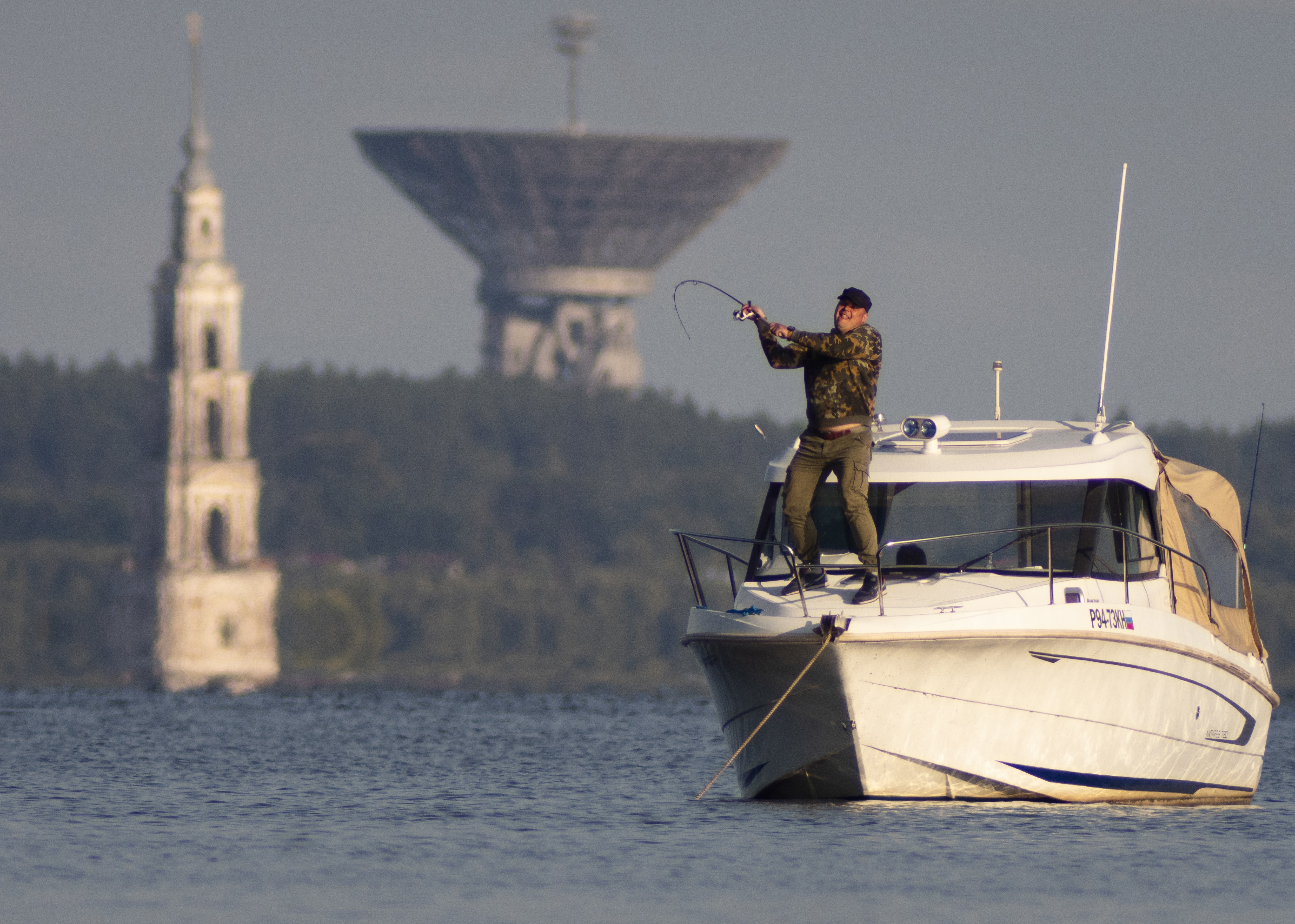In this Sunday, Aug. 11, 2019 photo a man fishes near the famous Kalyazin Bell Tower, part of the submerged monastery of St. Nicholas and giant antenna of the Kalyazin radio astronomy observatory in the town of Kalyazin located on the Volga River, 180 km (111 miles) north-east of Moscow, Russia. (AP Photo/Dmitri Lovetsky)