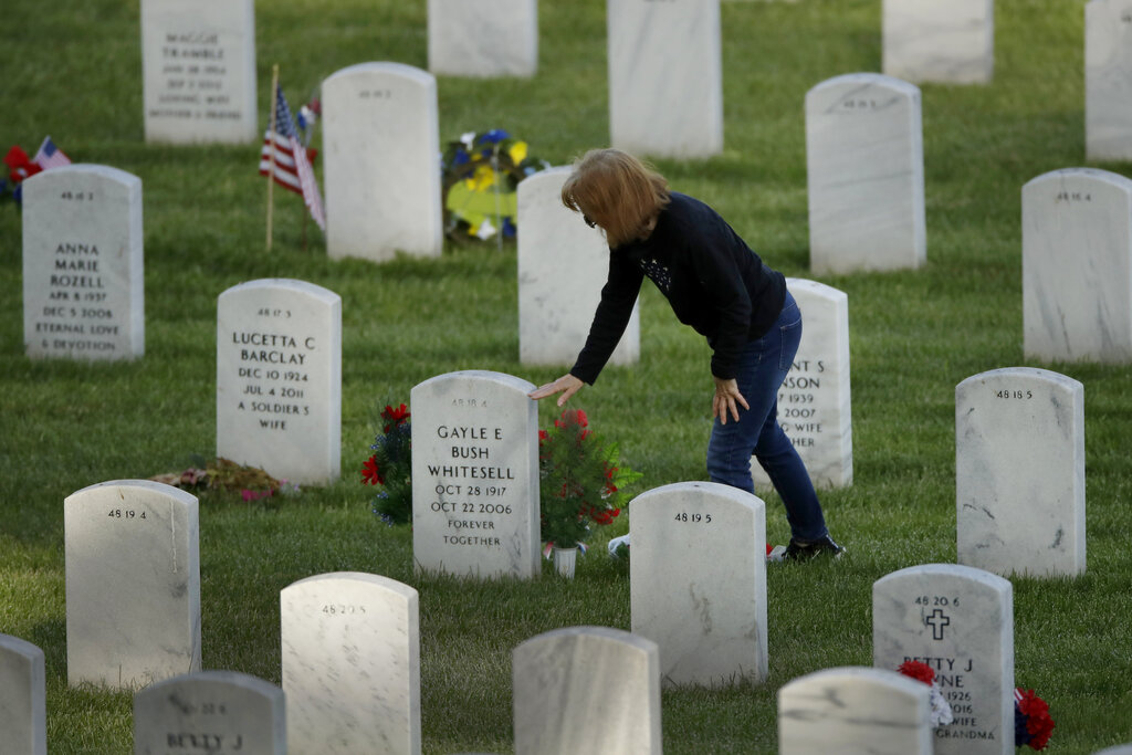 Pam Barba pauses at her parent's grave while visiting Leavenworth National Cemetery Saturday, May 23, 2020 in Leavenworth, Kan. Barba said she decided to visit to the cemetery today instead of Memorial Day to beat the crowd and minimize the chance of catching COVID-19. (AP Photo/Charlie Riedel)