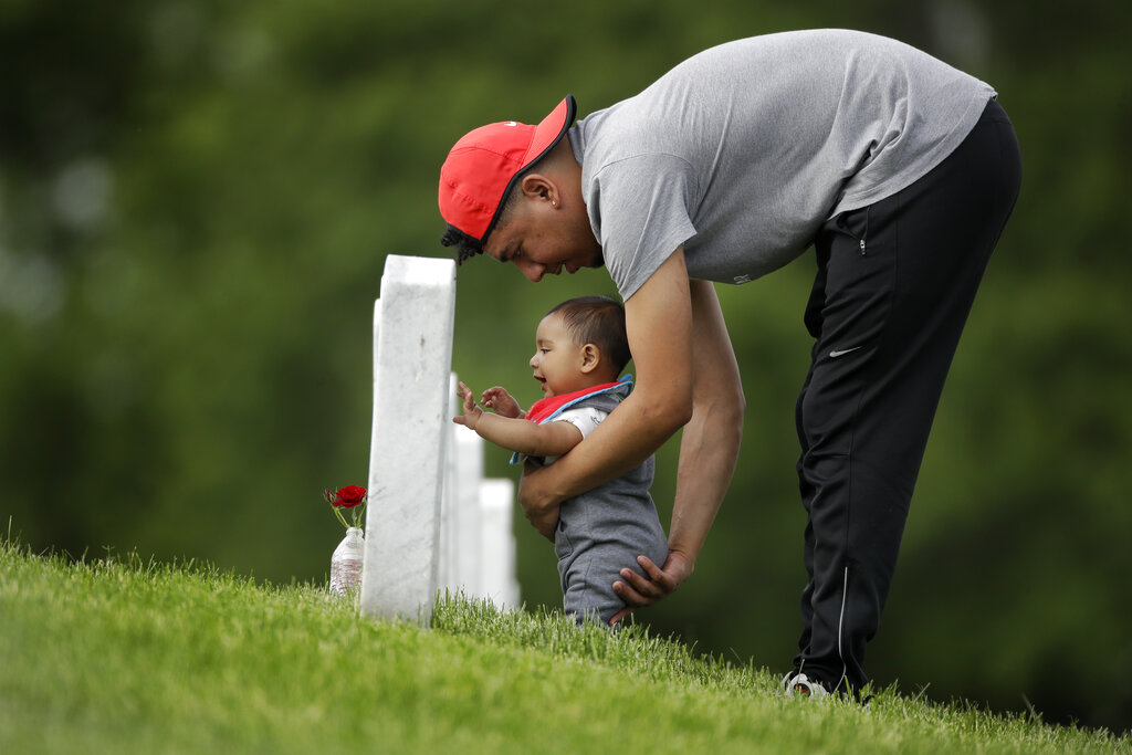 Angel Garcia-Metcalf steadies his seven-month-old son Angel as they visit the boy's great-grandfather's grave at Leavenworth National Cemetery Saturday, May 23, 2020 in Leavenworth, Kan. They were among a handful of people who decided to visit to the cemetery today instead of Memorial Day to beat the crowd and minimize the chance of catching COVID-19. (AP Photo/Charlie Riedel)
