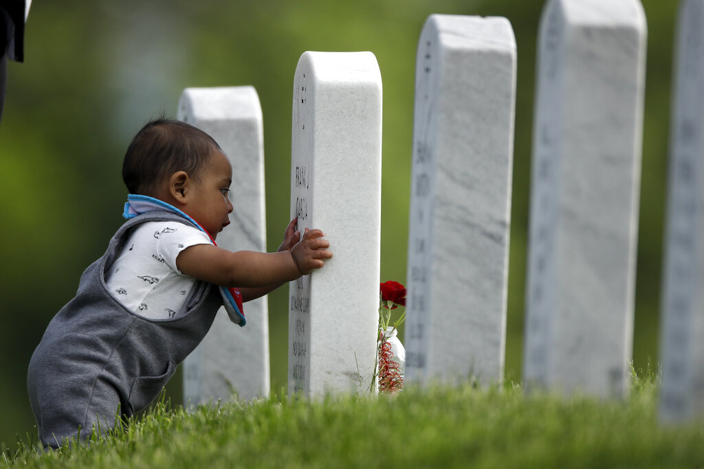 Seven-month-old son Angel Garcia-Metcalf looks at his great-grandfather's grave as he visits Leavenworth National Cemetery with his parents Saturday, May 23, 2020 in Leavenworth, Kan. They were among a handful of people who decided to visit to the cemetery today instead of Memorial Day to beat the crowd and minimize the chance of catching COVID-19. (AP Photo/Charlie Riedel)