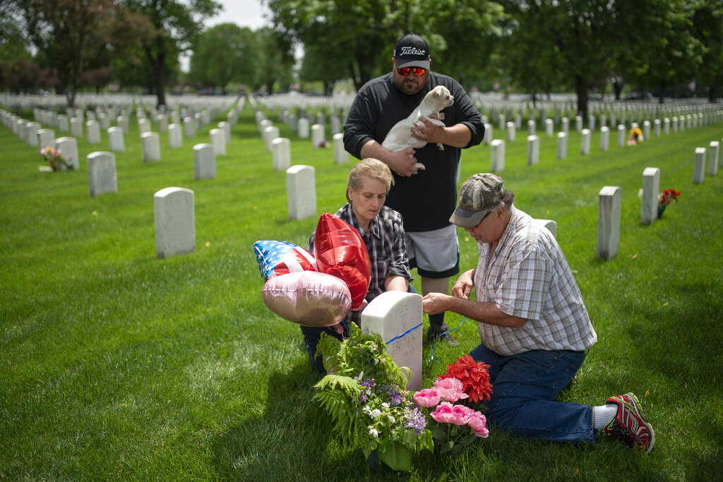 Teresa Baron places flowers and balloons at the headstone of her father, World War II Navy veteran Frank Baron, Sunday, May 24, 2020, at Fort Snelling Cemetery in Bloomington, Minn., during Memorial Day weekend. Teresa Baron's mother' and sister's remains are also buried at the cemetery. Her son Eddie Baron holds their dog 