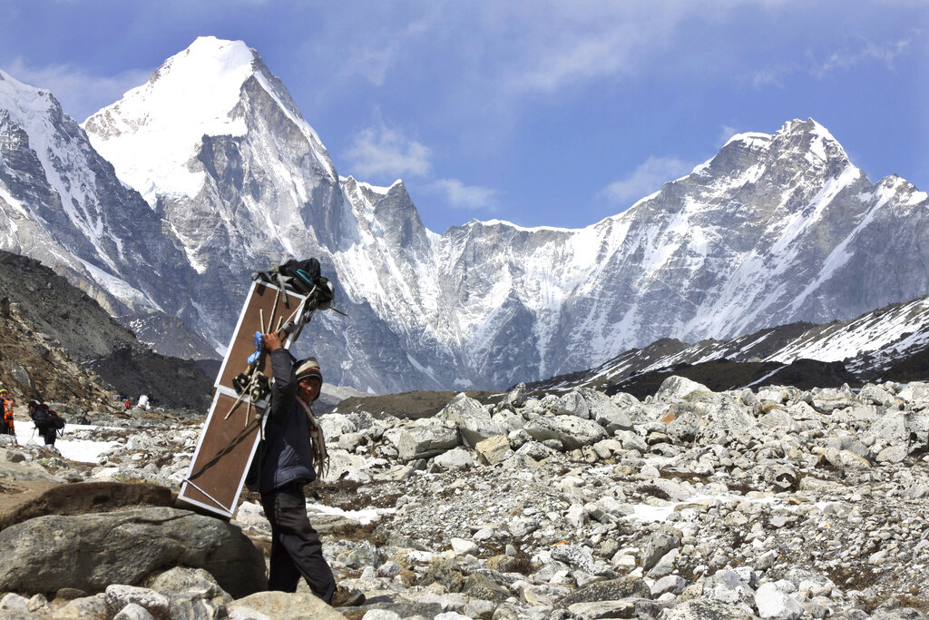FILE - In this Friday, April 10, 2015, file photo, a porter carries crates containing oxygen tanks, with Mt Lingtren seen behind left, and Mt. Khumbutse, right, on his way towards Everest Base Camp, at Lobuche, Nepal. China shut down the northern route through Tibet due to the COVID-19 pandemic on March 12. A day later, expeditions to the Nepal side were closed, too. The closure of Mount Everest will have significant financial ramifications for the local Sherpas, cooks, porters and other personnel who make their living during the short climbing window. (AP Photo/Tashi Sherpa, File)