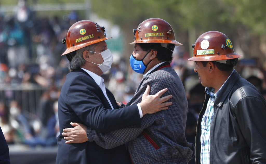 Wearing the work hats of Bolivian miners, Bolivia's former President Evo Morales, center, and Argentina's President Alberto Fernandez, left, embrace as they stand in the middle of the border bridge that connects the town of La Quiaca, Argentina with the town of Villazon, Bolivia, Monday, Nov. 9, 2020. Morales, who fled into exile after resigning last November, returned to his homeland the day after the presidential inauguration of his former finance minister Luis Arce. (AP Photo/Juan Karita)