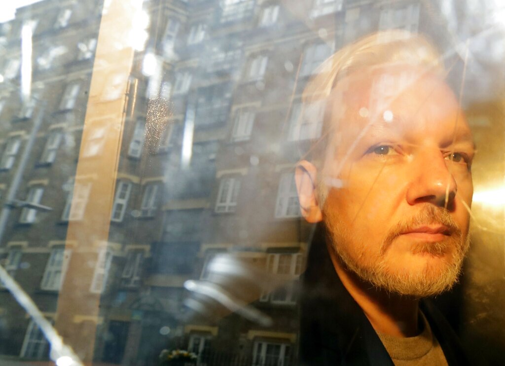 FILE - In this Wednesday May 1, 2019 file photo buildings are reflected in the window as WikiLeaks founder Julian Assange is taken from court, where he appeared on charges of jumping British bail seven years ago, in London. Assange relayed how he “binge-watched” the suicide of the former Bosnian Croat general in a U.N. courtroom three years ago, a doctor who visited the WikiLeaks founder on several occasions while he was in the Ecuadorian Embassy in London told an extradition hearing Thursday, Sept. 24, 2020. (AP Photo/Matt Dunham, File)