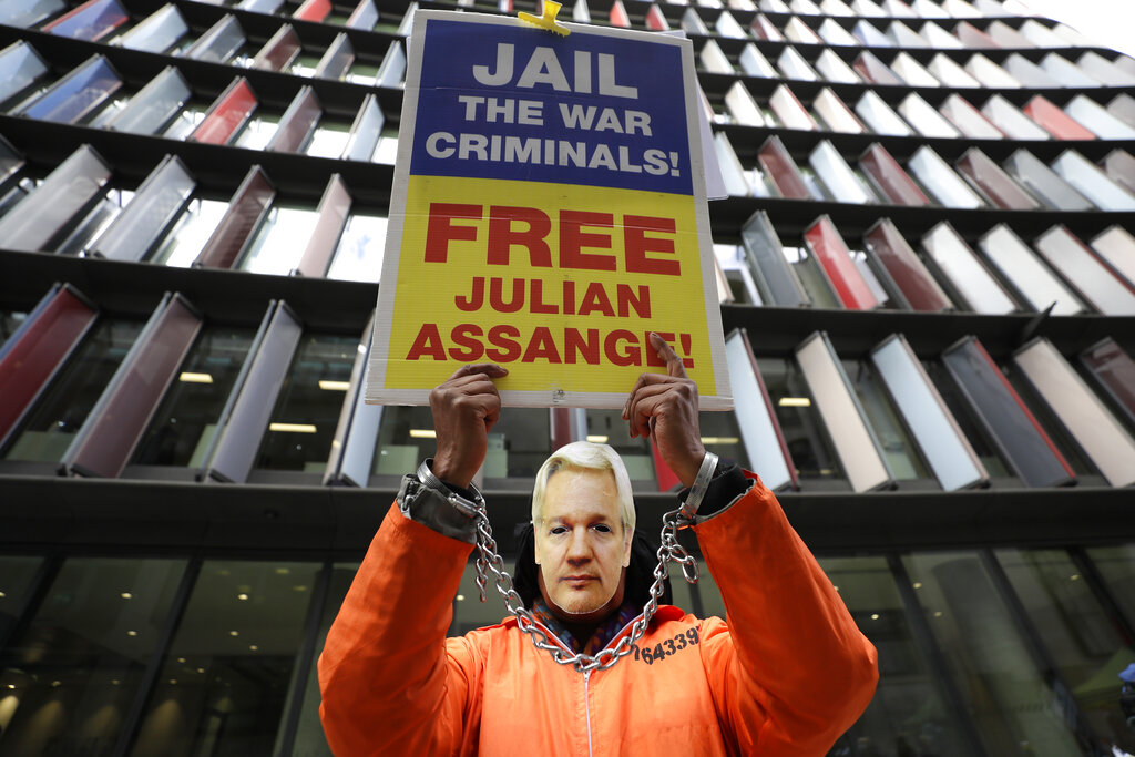 A demonstrator holds a banner and wears a Julian Assange mask opposite the Old Bailey in London, Thursday, Oct. 1, 2020, as the Julian Assange extradition hearing to the US continues. (AP Photo/Kirsty Wigglesworth)