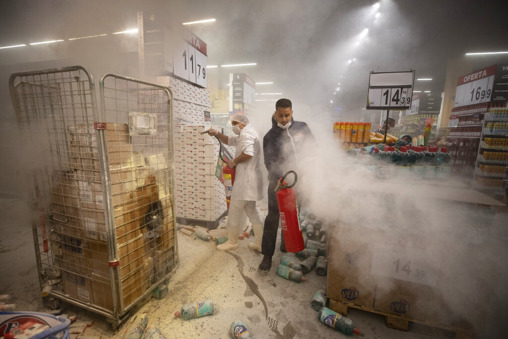 Employees douse a fire set by protesters inside a Carrefour supermarket during a protest against the murder of Black man Joao Alberto Silveira Freitas at a different Carrefour supermarket the night before, on Brazil's National Black Consciousness Day in Sao Paulo, Brazil, Friday, Nov. 20, 2020. Freitas died after being beaten by supermarket security guards in the southern Brazilian city of Porto Alegre, sparking outrage as videos of the incident circulated on social media.  (AP Photo/Andre Penner)