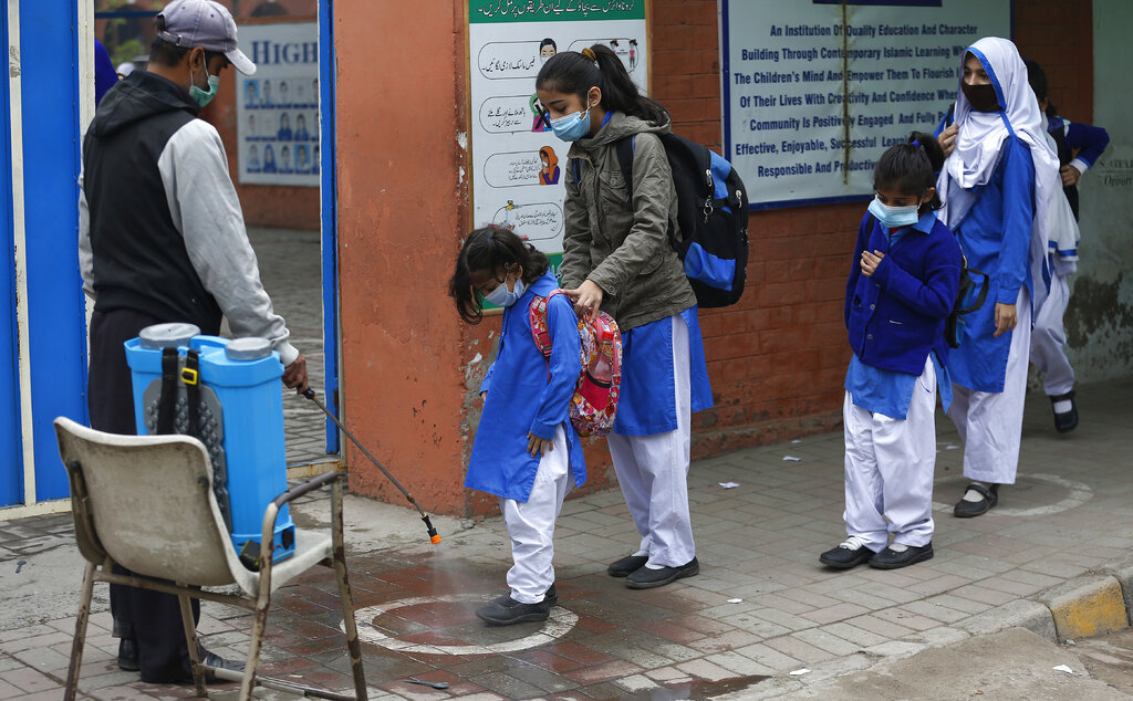 A worker sprays sanitizer on the shoes of students as they arrive at a school in Lahore, Pakistan, Wednesday, Nov. 25, 2020. Pakistan will again close all educational institutions as of Thursday Nov. 26, 2020, because of a steady and increasingly drastic increase in coronavirus cases. (AP Photo/K.M.Chaudary)