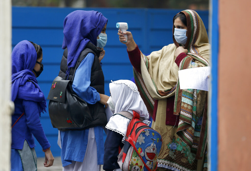A teacher checks body temperatures of students as they arrive at a school in Lahore, Pakistan, Wednesday, Nov. 25, 2020. Pakistan will again close all educational institutions as of Thursday Nov. 26, 2020, because of a steady and increasingly drastic increase in coronavirus cases.  (AP Photo/K.M.Chaudary)
