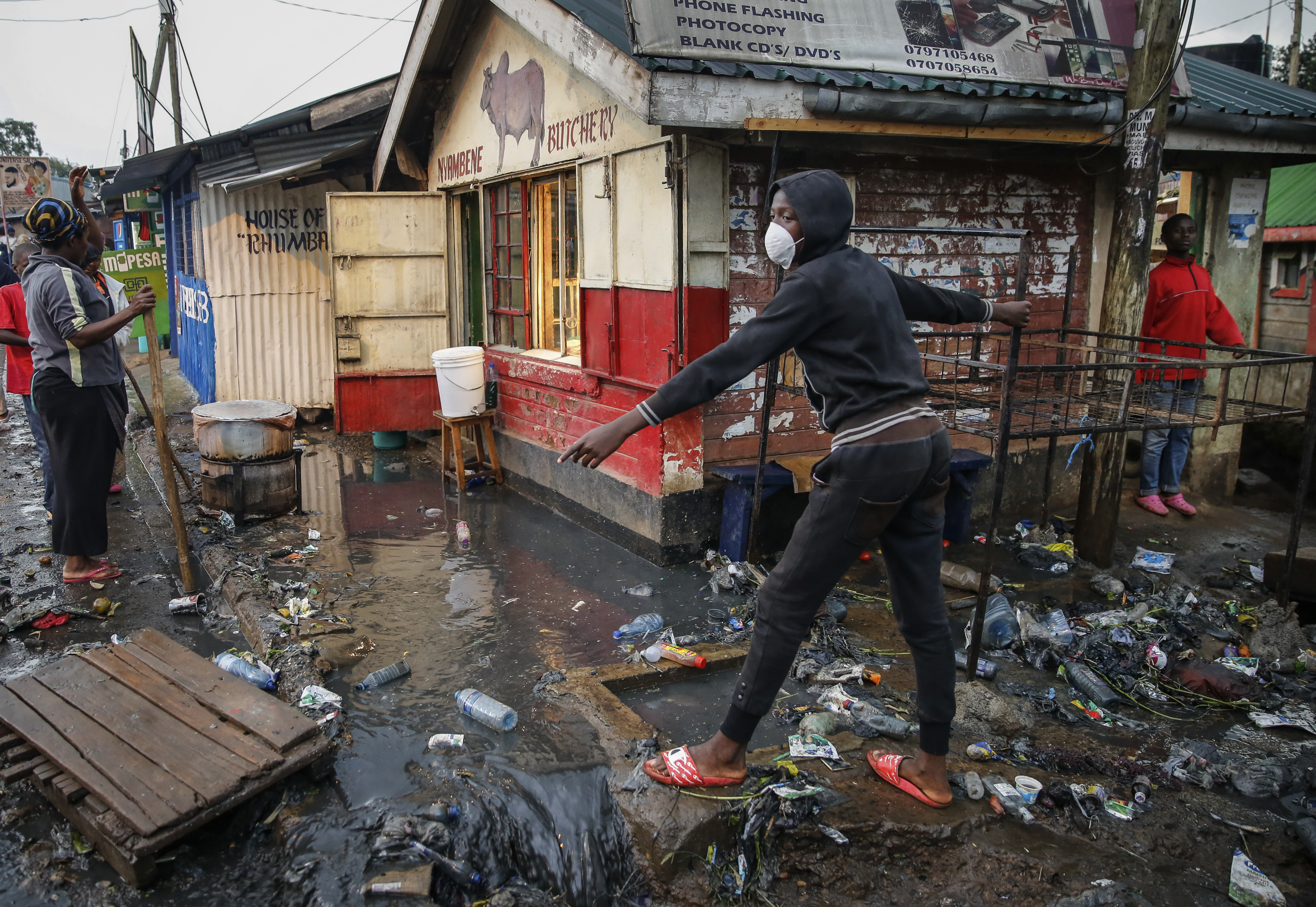 A boy wears a mask as a preventative measure against the spread of the new coronavirus, as he navigates floodwaters mixed with garbage following heavy rains, in the Kibera slum, or informal settlement, of Nairobi, Kenya, on Thursday, March 26, 2020. Many slum residents say staying at home or social-distancing is impossible for those who live hand to mouth and receive daily wages for informal work, as is maintaining sanitation in densely populated areas where a pit latrine can be shared by dozens. (AP Photo/Brian Inganga)
