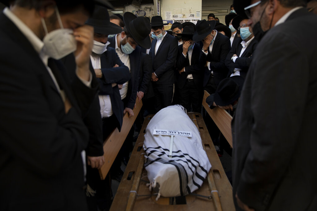 Ultra-orthodox Jewish men gather around the body of Rabbi Aharon David Hadash, the spiritual leader of the Mir Yeshiva, a prominent religious seminary, during his funeral in Jerusalem, Thursday, Dec. 3, 2020. The mass ceremony took place despite coronavirus restrictions limiting the size of funerals. Hadash, who was 90 was hospitalized two months ago after he tested positive for COVID-19. (AP Photo/Oded Balilty)