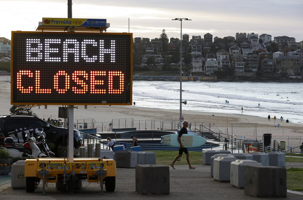 A sign indicates that Bondi Beach is closed as a surfer arrives for the 7 a.m. opening in Sydney, Tuesday, April 28, 2020, as coronavirus pandemic restrictions are eased. The beach is open to swimmers and surfers to exercise only. (AP Photo/Rick Rycroft)
