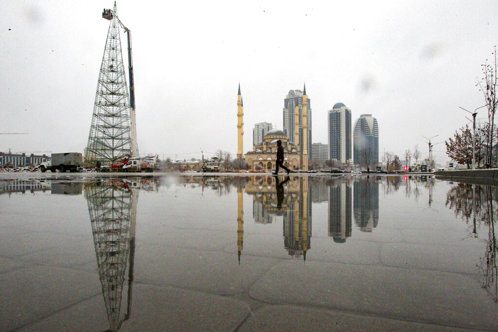A man walks through a square after snowfall as workers assemble a Christmas tree, with the main Mosque and skyscrapers in the background in downtown Grozny, the capital of Chechnya, Russia, Sunday, Dec. 6, 2020. (AP Photo/Musa Sadulayev)