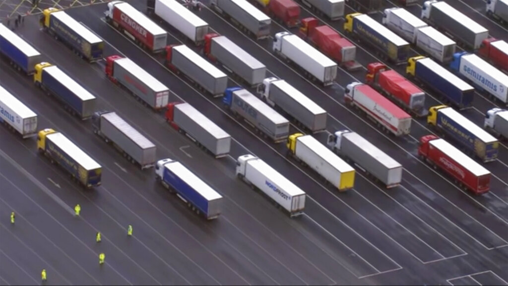Trucks are parked in a holding area, in this aerial photo taken from video, lined up at former airfield in Manston, England, close to the M20 highway that runs to the port of Dover, Britain's main ferry connection with mainland Europe in northern France, Tuesday Dec. 22, 2020. The goods trucks are waiting to get out of Britain as France barred travel from the UK for 48 hours because of a new and seemingly more contagious strain of the coronavirus in England. (Sky via AP)