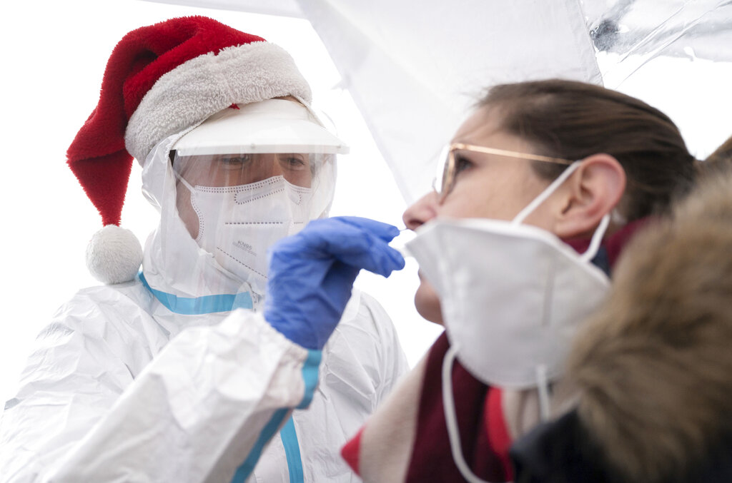 A volunteer DRK helper wearing a bobble hat performs a coronavirus rapid test on a woman at a testing station in Goppingen, Germany, Thursday, Dec. 24, 2020.  Just before Christmas, tens of thousands of people across the country can get tested for the corona virus to make sure they don't infect relatives or close friends when they give presents. Several aid services, such as the German Red Cross (DRK) and the Malteser, offer the campaign. (Marijan Murat/dpa via AP)