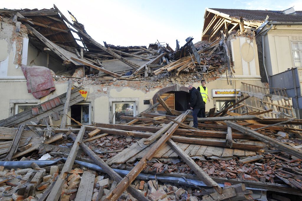People walk through the rubble from buildings damaged in an earthquake in Petrinja, Croatia, Tuesday, Dec. 29, 2020. A strong earthquake has hit central Croatia and caused major damage and at least one death and some 20 injuries in the town southeast of the capital Zagreb. (AP Photo)