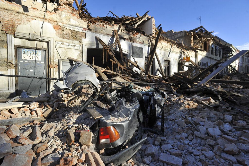 A view of remains of a car covered by debris and buildings damaged in an earthquake in Petrinja, Croatia, Tuesday, Dec. 29, 2020.  A strong earthquake has hit central Croatia and caused major damage and at least one death and 20 injuries in a town southeast of the capital Zagreb. (AP Photo)