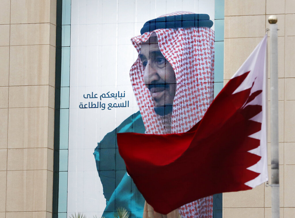 A Qatari flag flies in front of a banner showing Saudi King Salman with Arabic reads, 