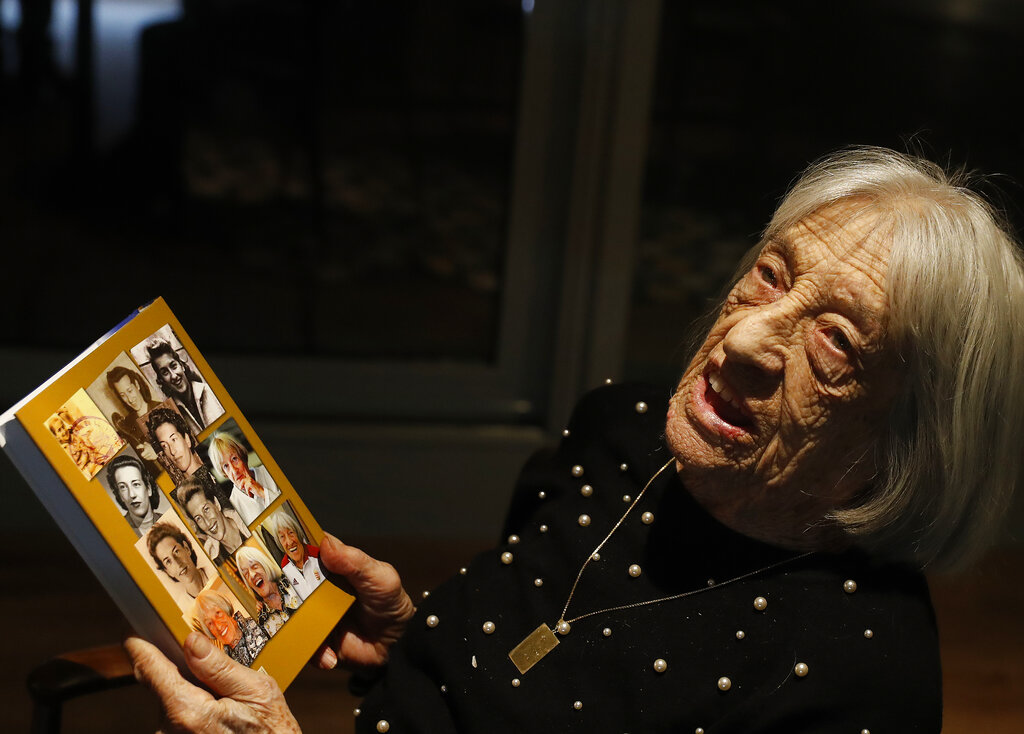 Agnes Keleti, former Olympic gold medal winning gymnast, holds a book with portraits of her on the back cover in Budapest, Hungary Monday Jan. 4, 2021. The oldest living Olympic champion turns 100 and says the fondest memory of her remarkable life is simply that she has lived through it all. Keleti had her illustrious career interrupted by World War II and the subsequent cancellation of the 1940 and 1944 Olympics. (AP Photo/Laszlo Balogh)