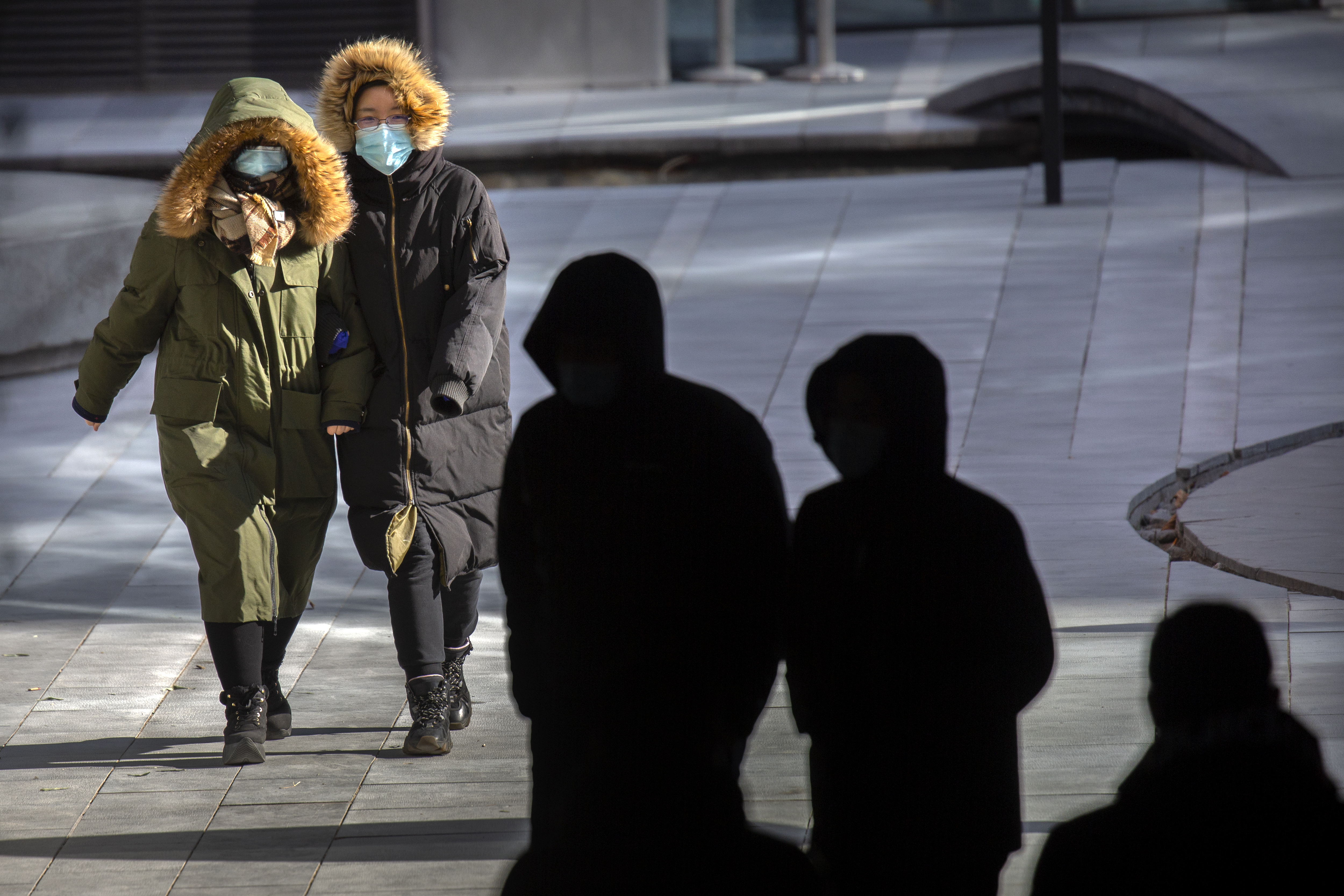 People wearing face masks to protect against the coronavirus walk on an unseasonably cold day at an office and shopping complex in Beijing, Wednesday, Jan. 6, 2021. China's Hebei province is enforcing stricter control measures following a further rise in coronavirus cases in the province, which is adjacent to the capital Beijing and is due to host events for next year's Winter Olympics. (AP Photo/Mark Schiefelbein)