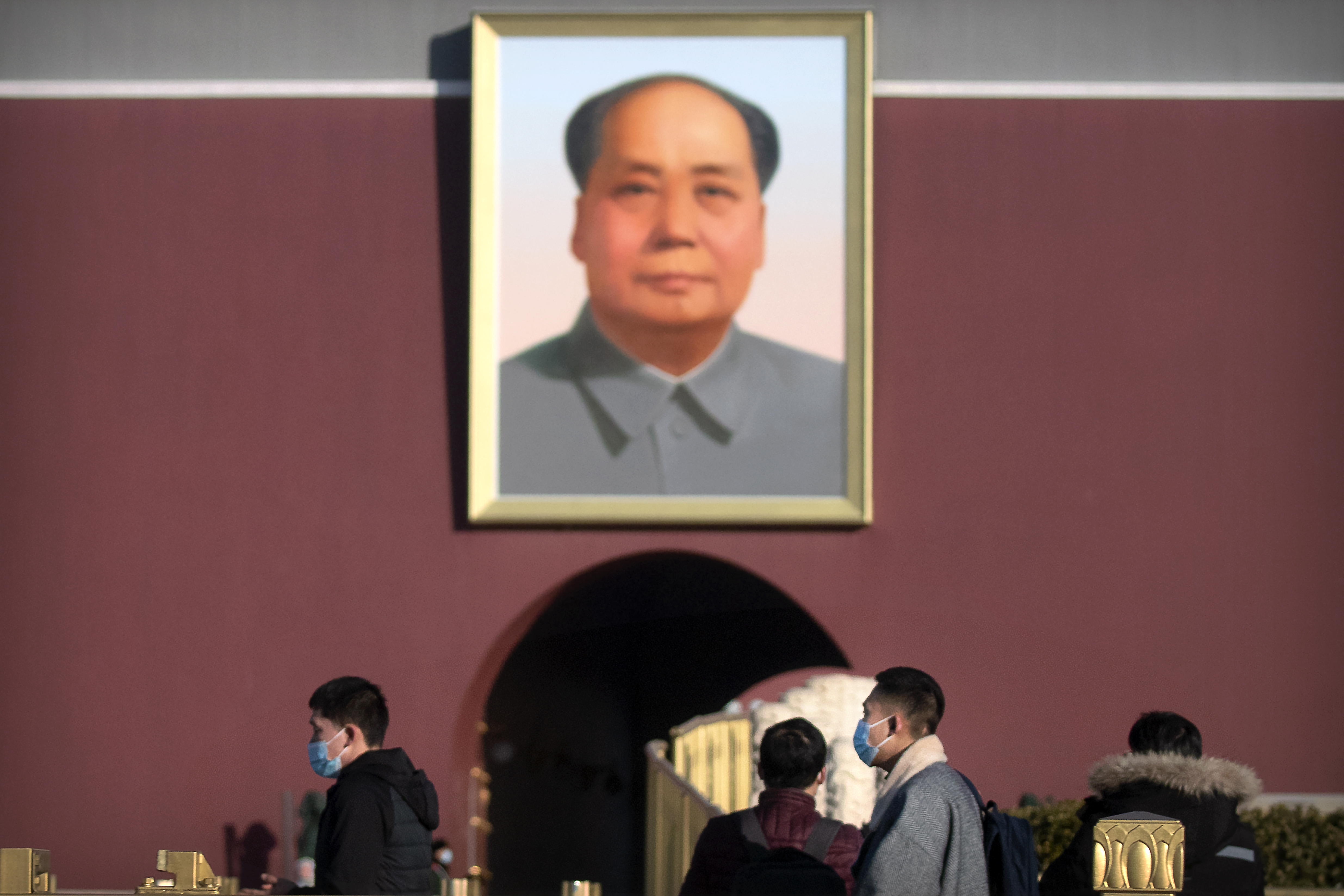 Visitors wearing face masks to protect against the spread of the coronavirus walk past the portrait of Chinese leader Mao Zedong on Tiananmen Gate near Tiananmen Square in Beijing, Saturday, Jan. 9, 2021. COVID vaccine shots will be free in China, where more than 9 million doses have been give to date, health officials in Beijing said Saturday. (AP Photo/Mark Schiefelbein)