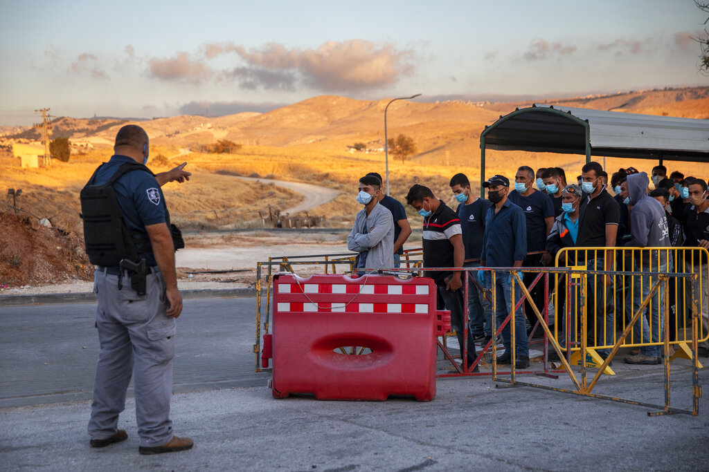 FILE - In this Tuesday, June 30, 2020, file photo,Palestinian laborers line up to cross a checkpoint at the entrance to the Israeli settlement of Maale Adumim, near Jerusalem. Israel's premier human rights group has begun describing both Israel and its control of the Palestinian territories as a single 
