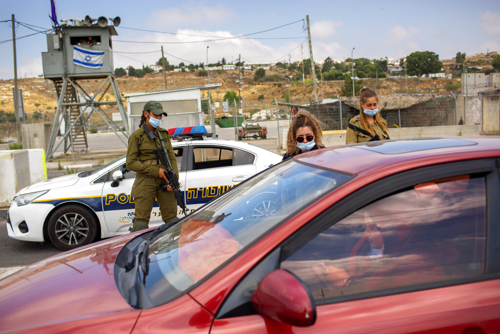 FILE - In this Tuesday, June 30, 2020 file photo, Israeli soldiers check the ID of a Palestinian woman at the Tapuach junction checkpoint next to the West Bank city of Nablus. Israel's premier human rights group has begun describing both Israel and its control of the Palestinian territories as a single 