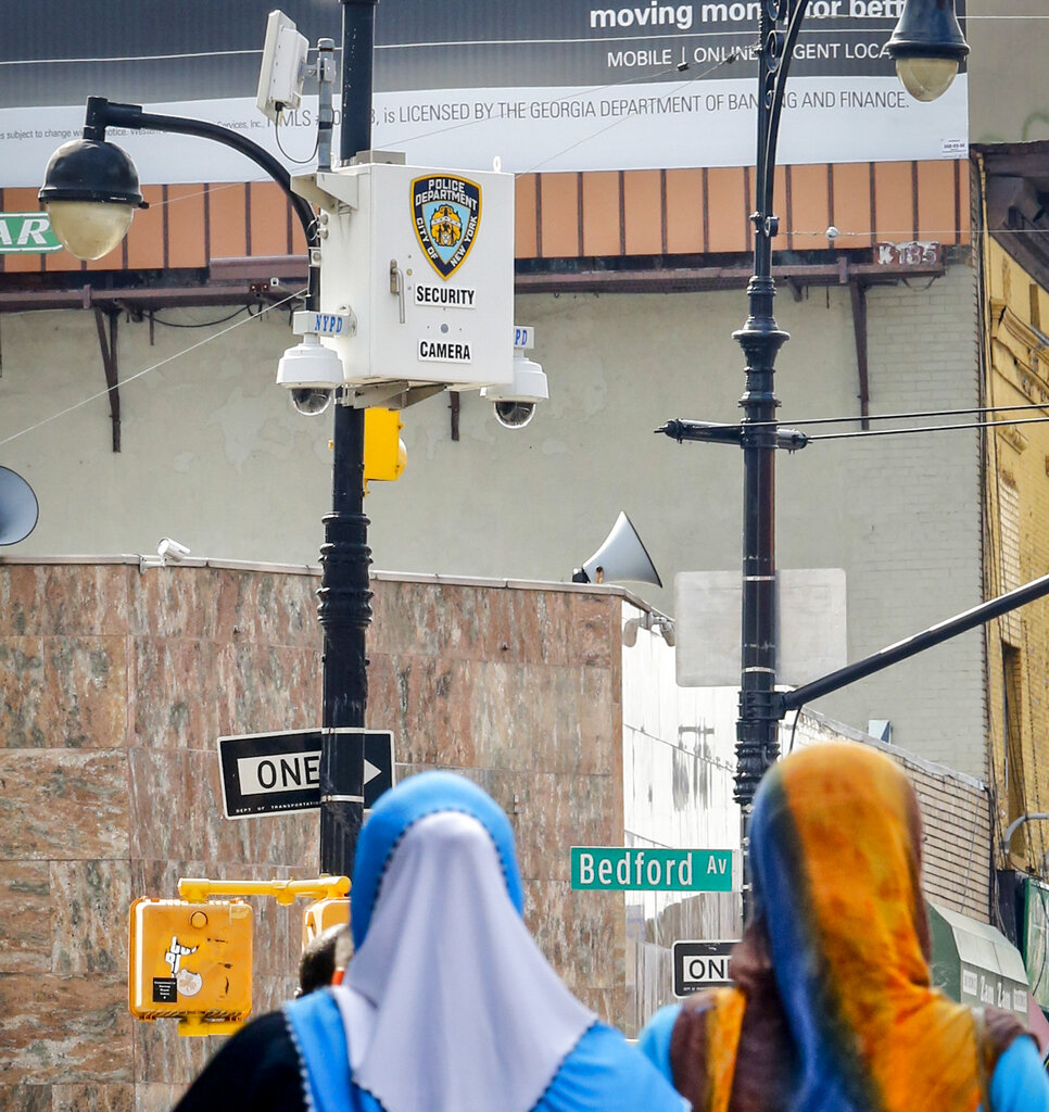 FILE - This photo from Friday Aug. 19, 2016, shows police surveillance cameras, top, on a light post overlooking the area of the Masjid At-Taqwa mosque at Bedford and Fulton Streets in Brooklyn, N.Y. Amnesty International is calling on New York City and state officials to ban law enforcement from using facial recognition technology, saying it threatens the civil rights of 