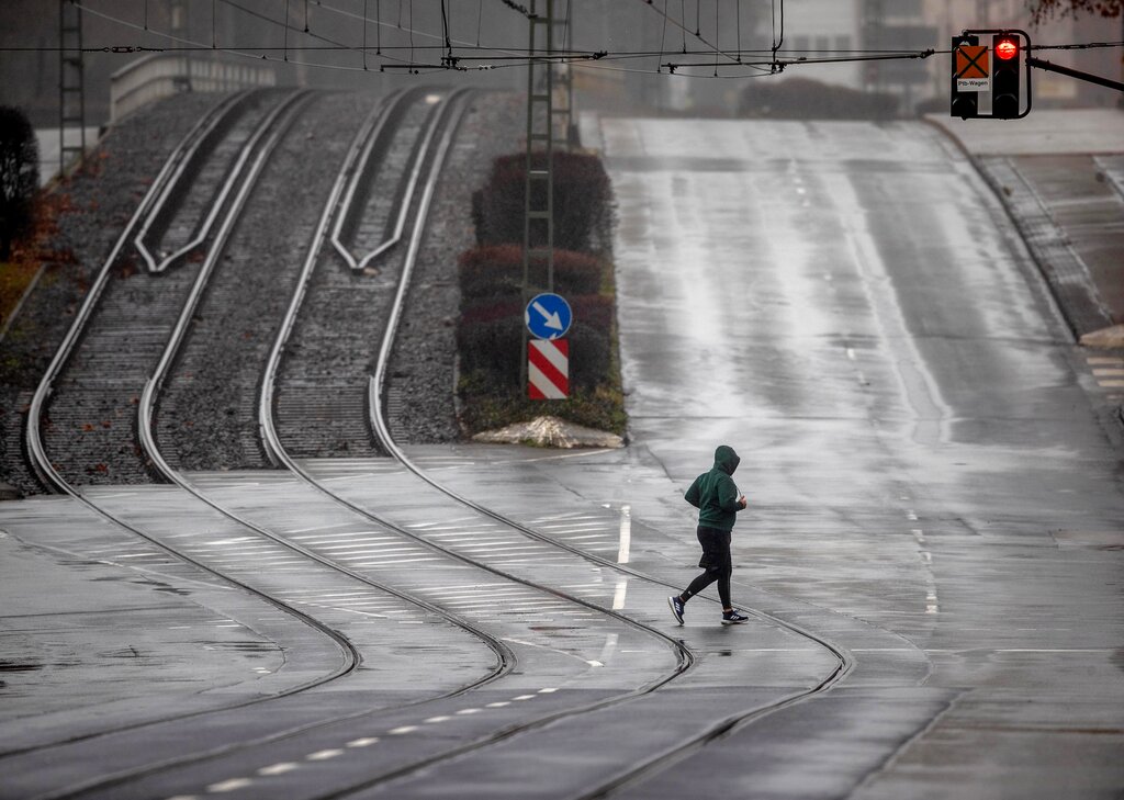 A man runs over an empty street with tram rails in Frankfurt, Germany, on a rainy Tuesday, Feb. 2, 2021. (AP Photo/Michael Probst)