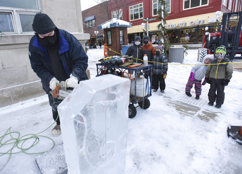 Children watch as ice carver Chad Hartson, of Napoleon, Ohio, begins a sculpture during the start of the 2021 Magical Ice Fest, Friday, Feb. 5, 2021, in downtown St. Joseph, Mich. (Don Campbell/The Herald-Palladium via AP)