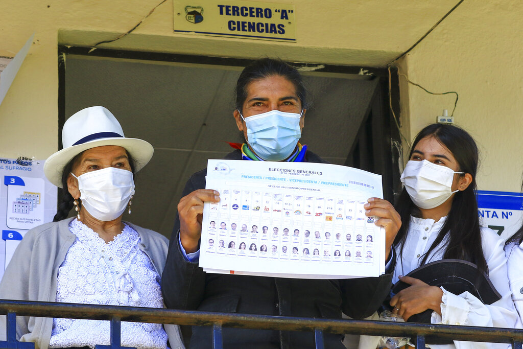 Flanked by his mother, left, and his daughter, wearing masks to protect form the new coronavirus, Yaku Perez, presidential candidate representing the Indigenous party Pachakutik, shows his ballot before voting in the presidential election, in Tarqui, Ecuador, Sunday, Feb. 7, 2021. (AP Photo/Marcelo Suquilanda)