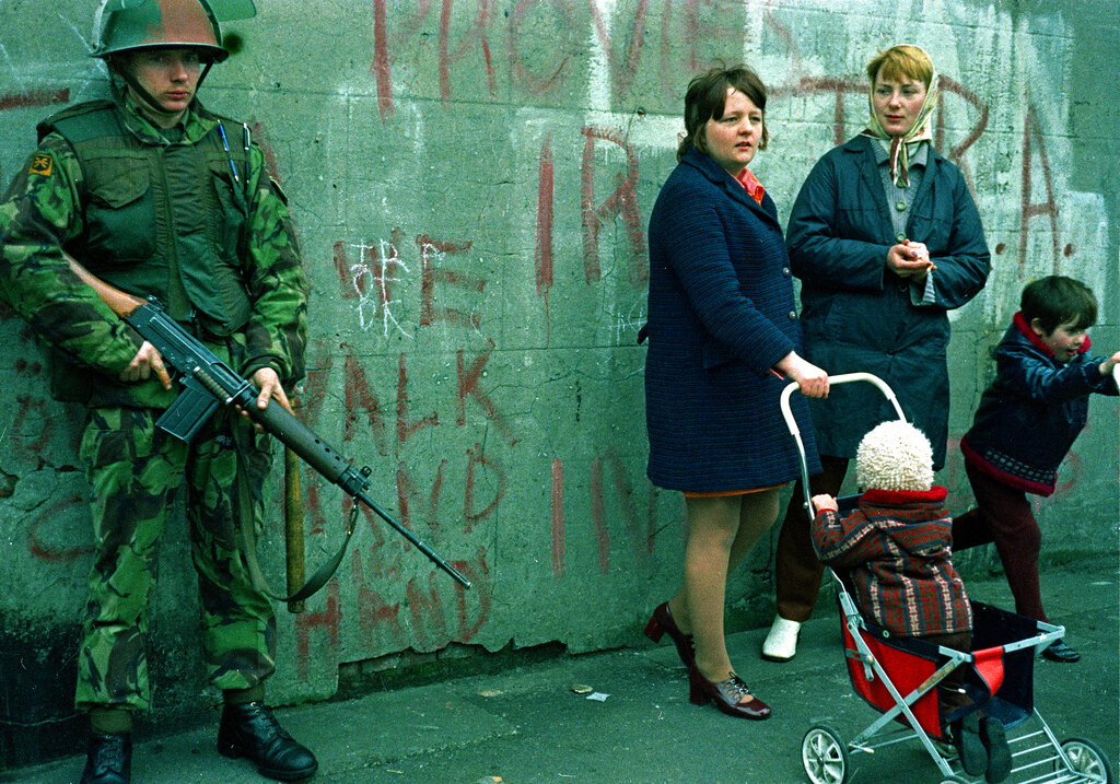 Women and children stand near an armed British military soldier patrols a street in Belfast, Northern Ireland, Feb. 1972.  British paratroopers shot 13 demonstrators during a civil rights march on Jan. 30, known as Bloody Sunday.  (AP Photo/Michel Laurent)