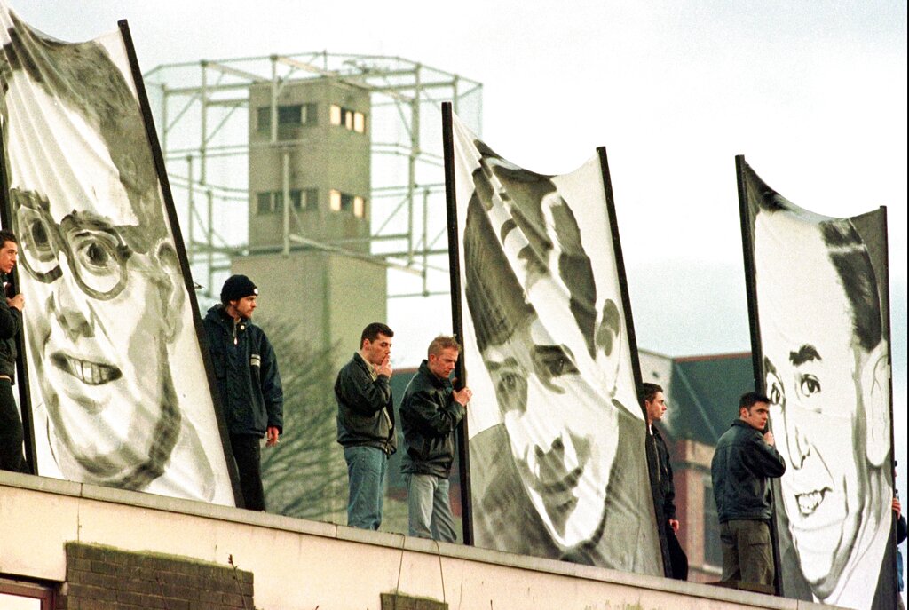 File - Protestors hold banners showing portraits of three of the thirteen killed on Bloody Sunday, against a backdrop of a security tower in this Sunday, Feb. 1, 1998 file photo, in Londonderry, Northern Ireland. The rally was held to honor the Irish demonstrators killed during a civil rights march in 1972.  Chief Constable Matt Baggott told Northern Irelands policing board Thursday July 5 2012  that his force is planning a Bloody Sunday investigation that would require 30 detectives and take four years.  Northern Irelands police commander says his detectives will eventually investigate the Bloody Sunday massacre to determine whether any British soldiers should be charged with murder _ but not yet.  Families of the 13 people killed when troops opened fire on Irish Catholic demonstrators in 1972 have waited for a criminal investigation to start since 2010, when the biggest fact-finding probe in British history determined that the soldiers targeted unarmed civilians. (AP Photo/Paul McErlane, File)