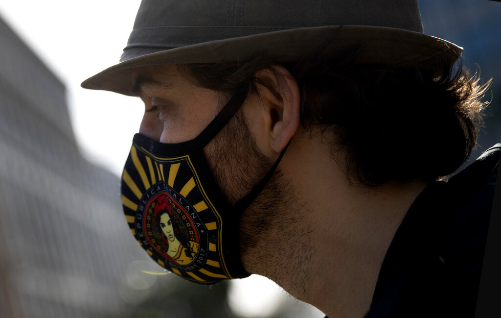 A demonstrator wears a protective face mask decorated in the colors of Catalonia as he takes part in a protest condemning the arrest of rap artist Pablo Hasel in Brussels, Tuesday, Feb. 23, 2021. The imprisonment of rap artist Pablo Hasel, for his music and tweets praising terrorist violence and insulting the Spanish monarchy, has set off a powder keg of pent-up rage this week in Spain. (AP Photo/Virginia Mayo)
