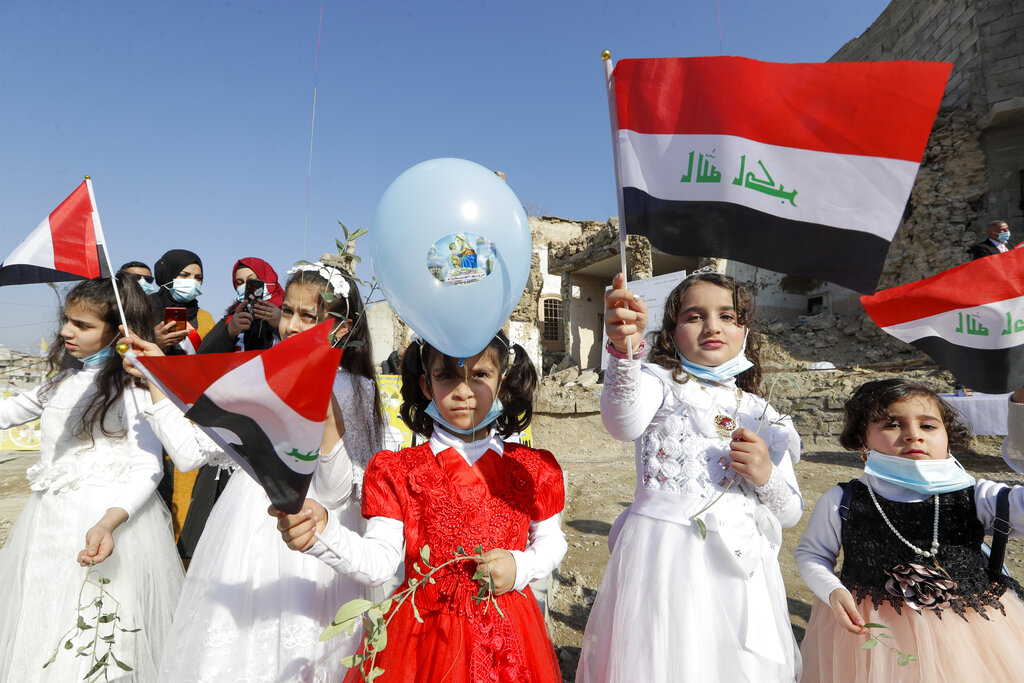 Children in their festive garment wave Iraqi flags to the camera as they arrive to join Pope Francis who will pray for the victims of war at Hosh al-Bieaa Church Square, in Mosul, Iraq, once the de-facto capital of IS, Sunday, March 7, 2021. The long 2014-2017 war to drive IS out left ransacked homes and charred or pulverized buildings around the north of Iraq, all sites Francis visited on Sunday. (AP Photo/Andrew Medichini)