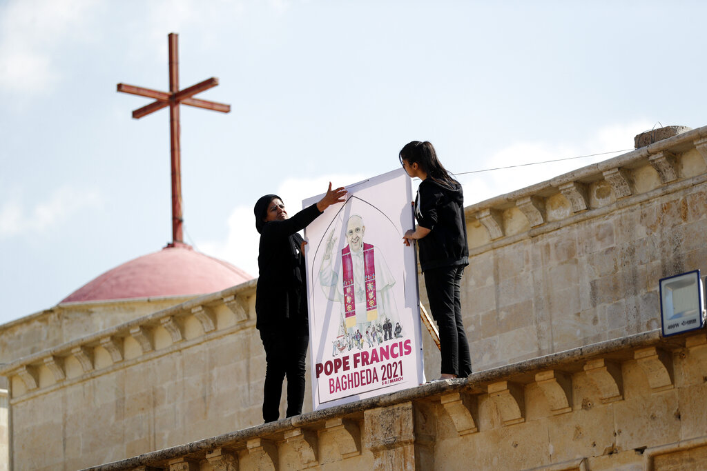 Iraqi Christians place a poster at Church of the Immaculate Conception in Qaraqosh, Iraq Tuesday, Feb. 23, 2021.  Pope Francis will visit the church during his historic trip to Iraq.   Damaged during the Islamic State reign of terror, the church's tragedy mirrored that of its Christian community which was devastated by the group. (AP Photo/Hadi Mizban)